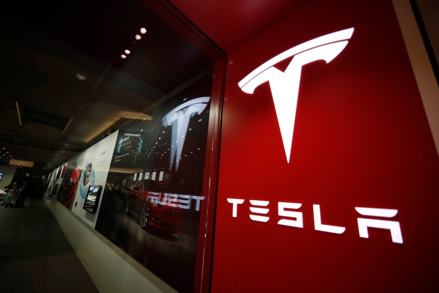 This Feb. 9, 2019, file photo shows a sign bearing the company logo outside a Tesla store in Cherry Creek Mall in Denver. A Tesla using its partially automated driving system slammed into a Florida Highway Patrol cruiser Saturday, Aug. 28, 2021 on an interstate near downtown Orlando and narrowly missed its driver, who had pulled over to assist a disabled vehicle. (AP Photo/David Zalubowski, File)