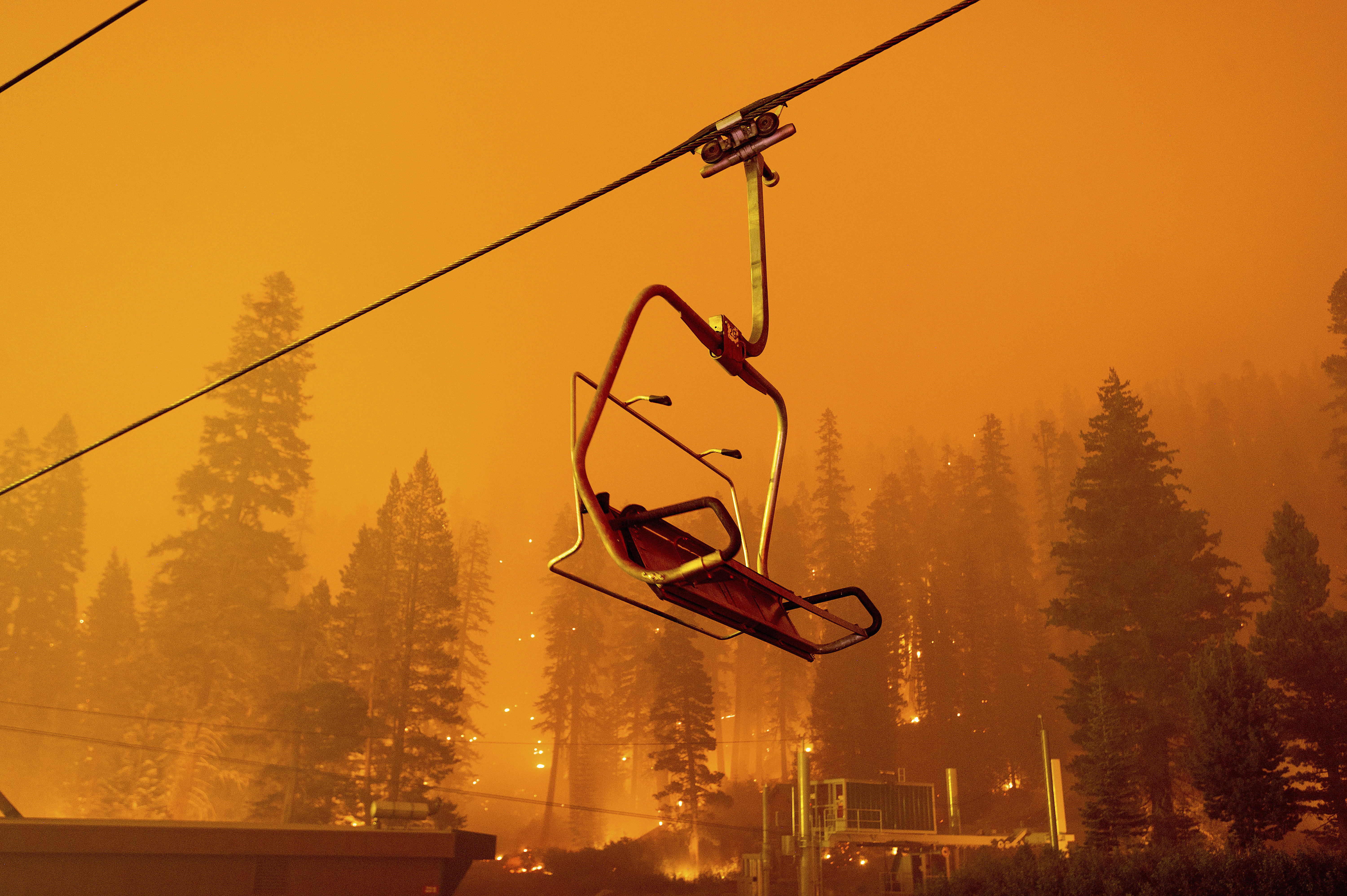 Seen in a long camera exposure, the Caldor Fire burns as a chairlift sits motionless at the Sierra-at-Tahoe ski resort on Aug. 29, 2021, in Eldorado National Forest. The main buildings at the ski slope's base survived as the main fire front passed. (Noah Berger / Associated Press)