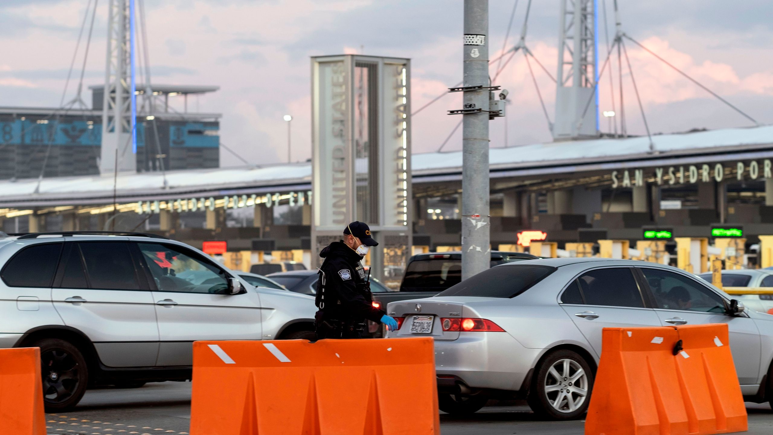 A Customs and Border Protection agent wears a face mask as he walks near cars lining up to cross to the United States at San Ysidro port of entry on March 21, 2020. (GUILLERMO ARIAS/AFP via Getty Images)