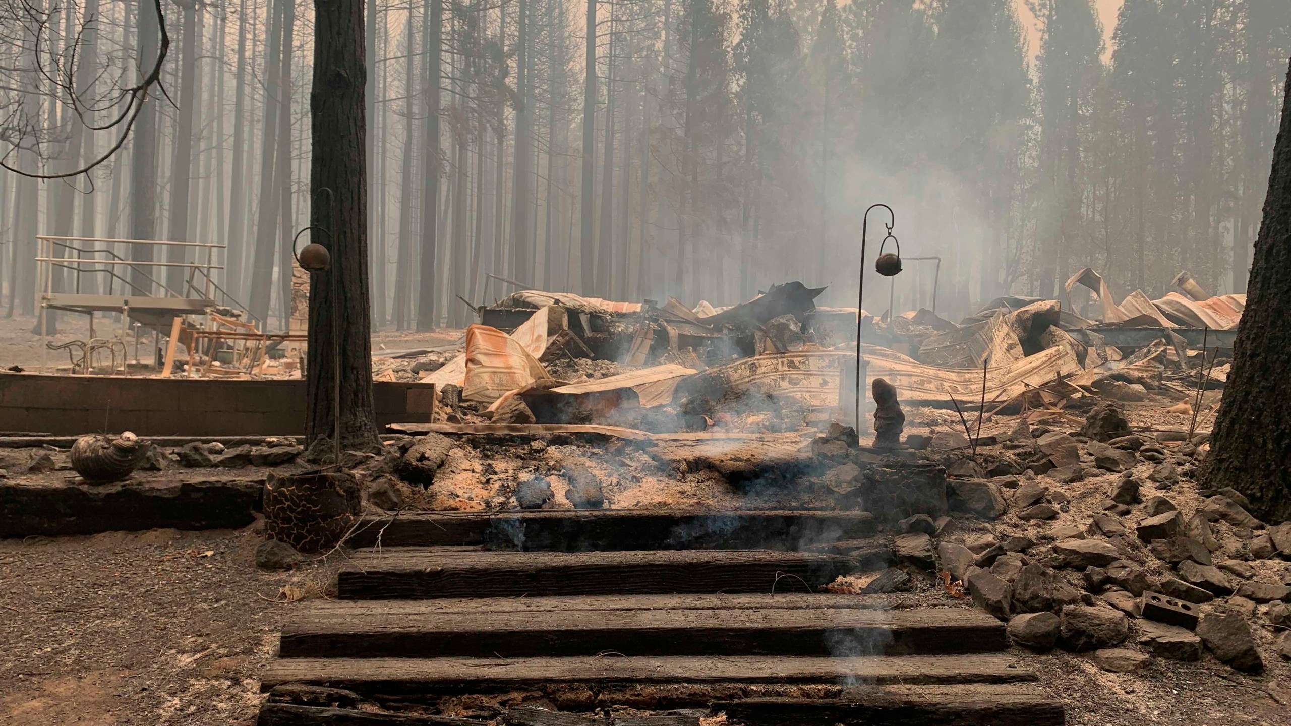 Smoke comes out under the front steps of a house that burned along North Arm Road in Plumas County near Taylorsville, Calif., Sunday, Aug. 15, 2021. (AP Photo/Eugene Garcia)