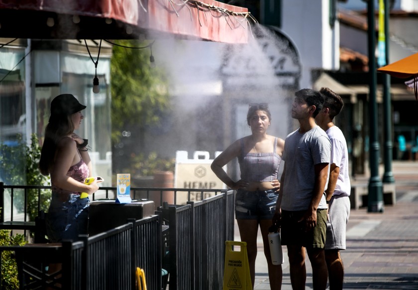 People cool off under a mister in downtown Palm Springs as the temperature soared to 110 degrees in July 2021. (Gina Ferazzi / Los Angeles Times)