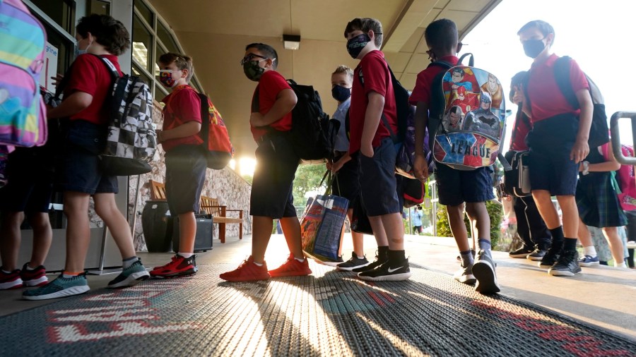 In this Aug. 17, 2021, file photo, wearing masks to prevent the spread of COVID-19, elementary school students line up to enter school for the first day of classes in Richardson, Texas. As COVID-19 cases surge, a majority of Americans say they support mask mandates for students and teachers in K-12 schools, but their views are sharply divided along political lines. (AP Photo/LM Otero, File)