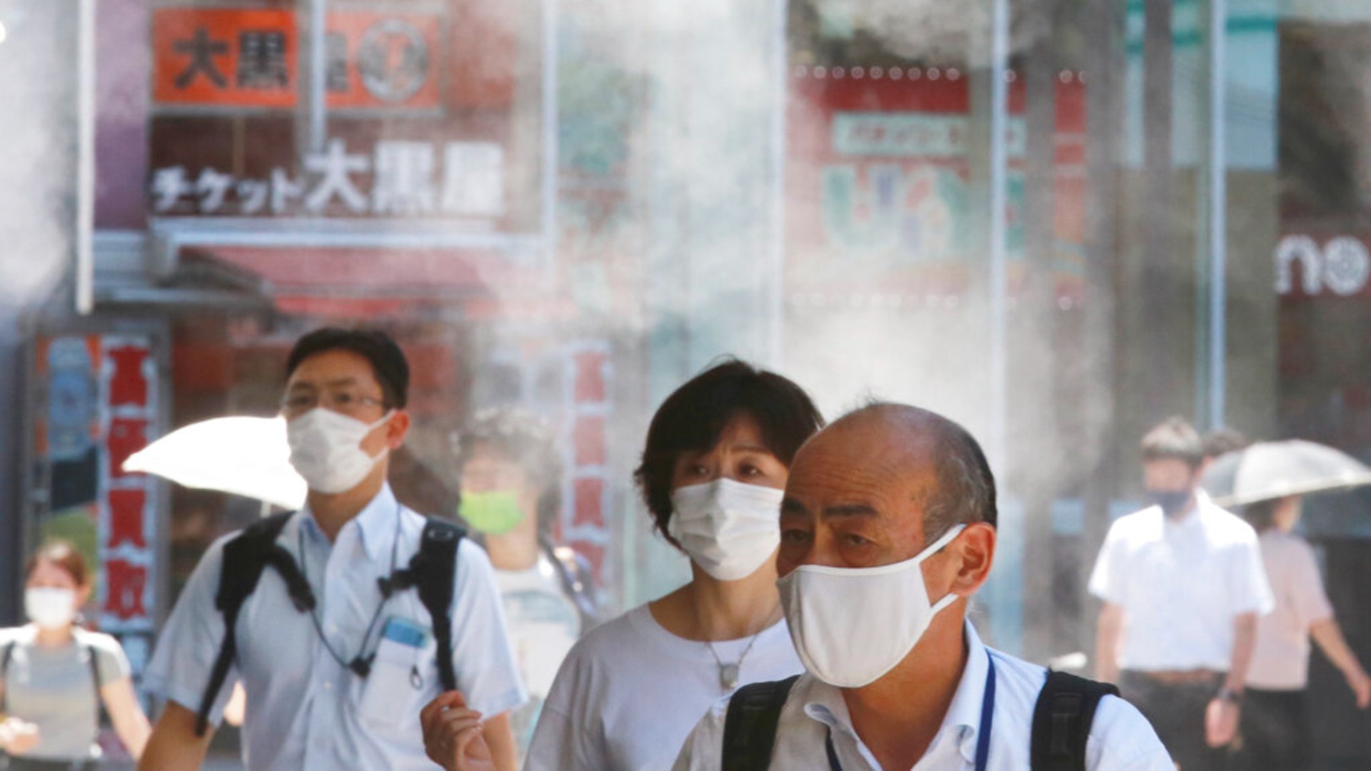 People wearing face masks to protect against the spread of the coronavirus walk under a water mist in Tokyo Thursday, Aug. 5, 2021. (AP Photo/Koji Sasahara)