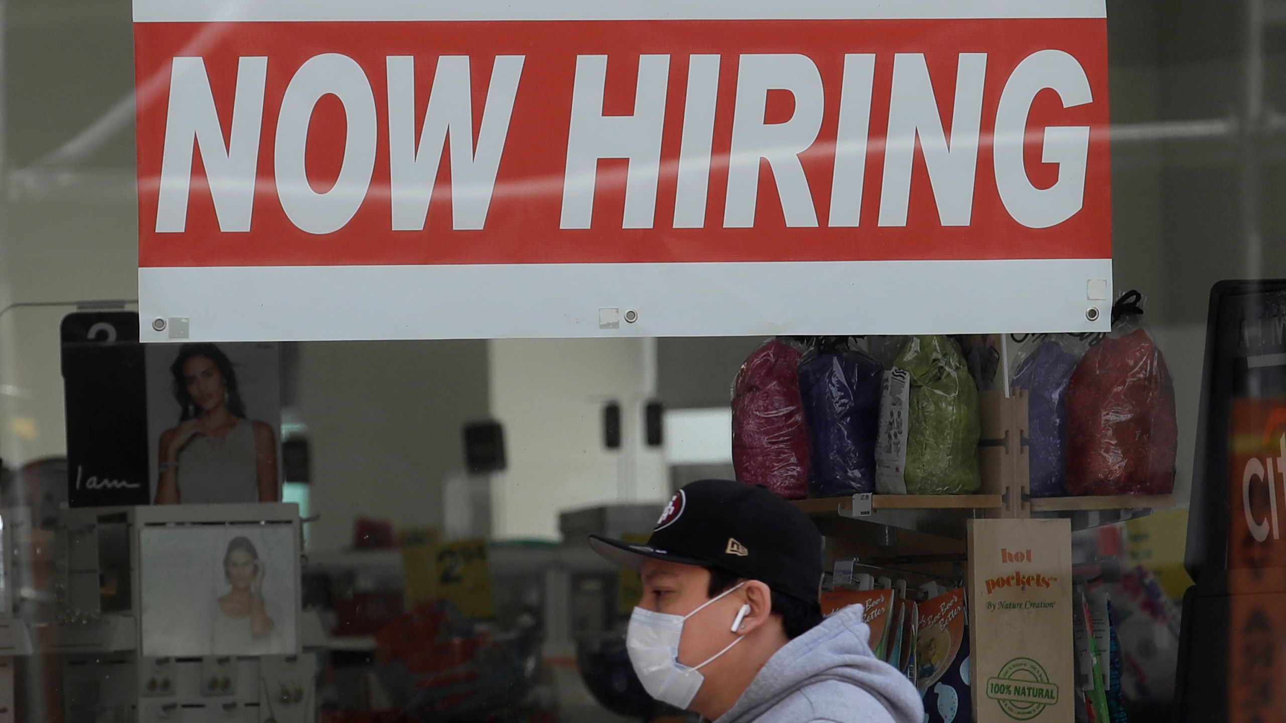 This May 7, 2020, file photo shows a man wearing a mask while walking under a Now Hiring sign at a CVS Pharmacy during the coronavirus outbreak in San Francisco. (AP Photo/Jeff Chiu, File)