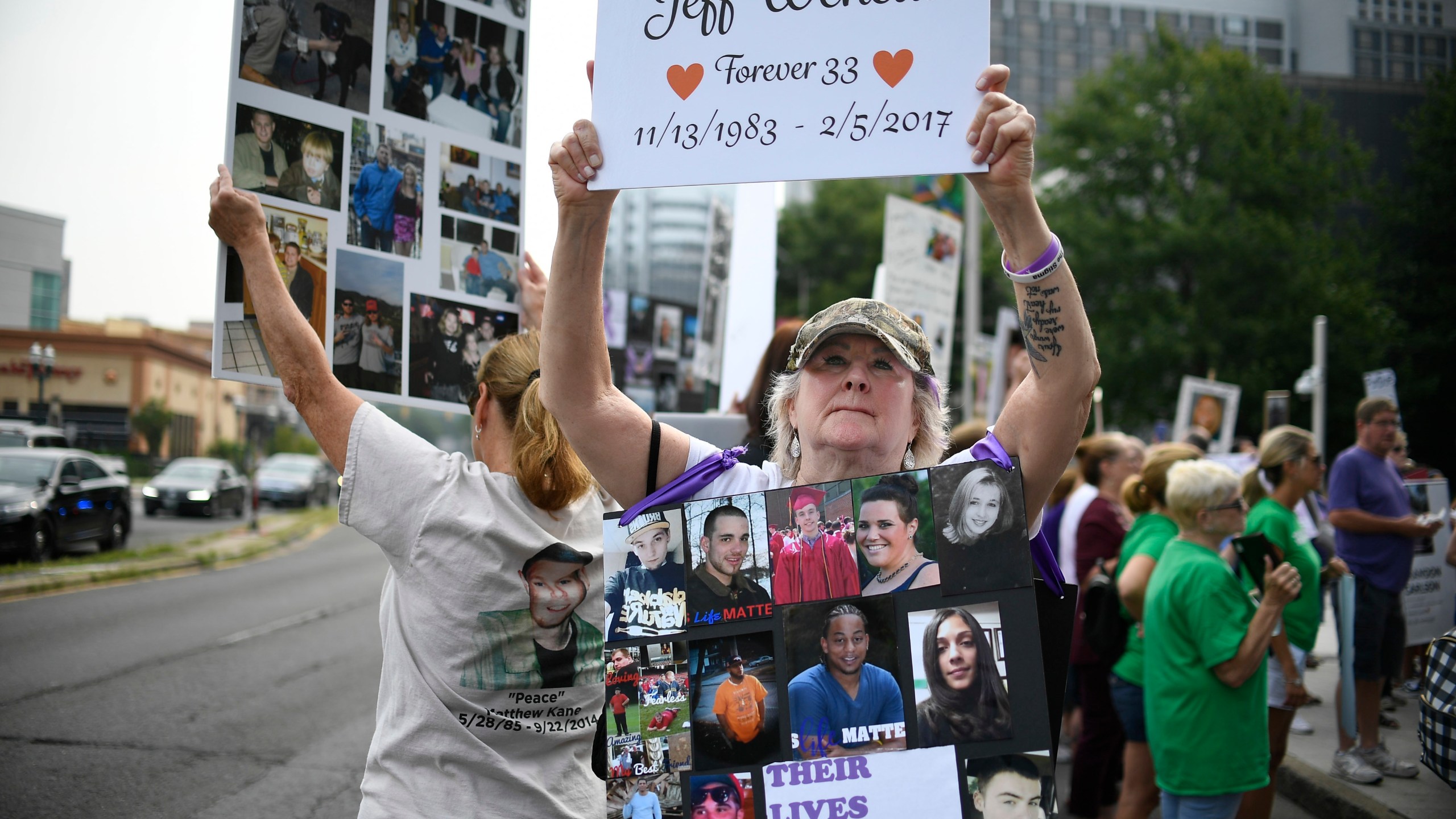 In this Aug. 17, 2018, file photo, Lynn Wencus of Wrentham, Mass., holds a sign with a picture of her son Jeff and wears a sign of others' loved ones lost to OxyContin and other opioids during a protest at Purdue Pharma LLP headquarters in Stamford, Conn. A landmark settlement in the nation’s opioid epidemic is forcing the owners of OxyContin maker Purdue Pharma to give up the company and pay out $4.5 billion. “Am I happy they don’t have to admit guilt and give up all their money? Of course not,” said Wencus. “But what would that do? It doesn’t bring my son back and it doesn’t help those who are suffering." (AP Photo/Jessica Hill, File)