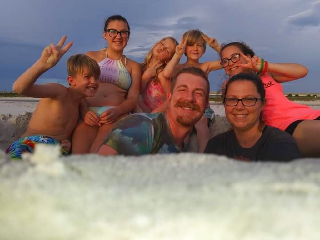 This 2019 photo provided by Cristina Miles shows Cristina Miles, Austin Miles and their five children at Matanzas Inlet in Florida, Florida is in the grip of its deadliest wave of COVID-19 since the pandemic began, a disaster driven by the highly contagious delta variant. Cristina Miles is among those facing more than one loss at once. (Cristina Miles via AP)