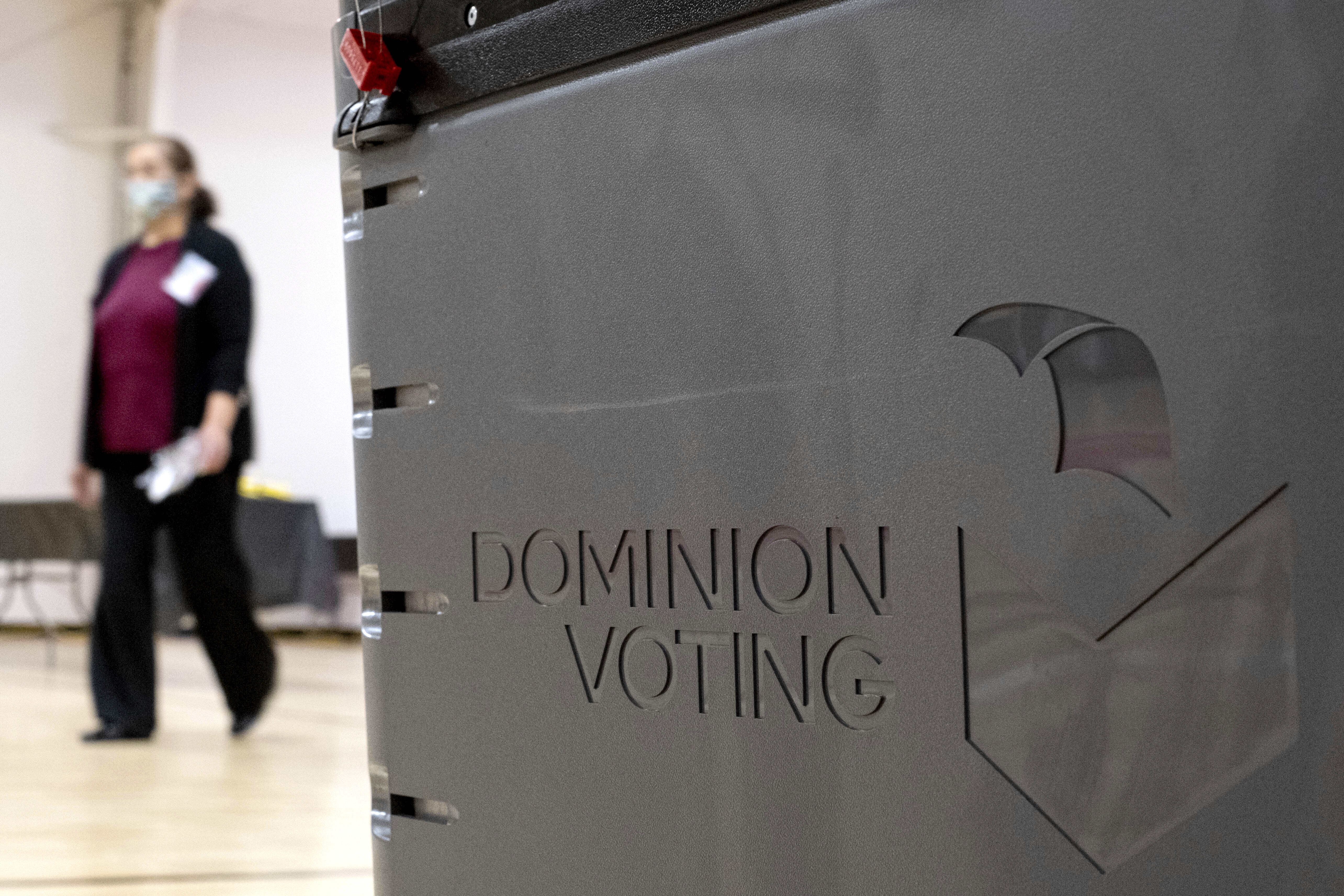 In this Jan. 4, 2021, file photo a worker passes a Dominion Voting ballot scanner while setting up a polling location at an elementary school in Gwinnett County, Ga., outside of Atlanta. A group of election security experts will ask California officials, Thursday, Sept. 2, to take additional steps to protect the upcoming governor’s recall election after the unauthorized release of voting system software in other states. (AP Photo/Ben Gray, File)