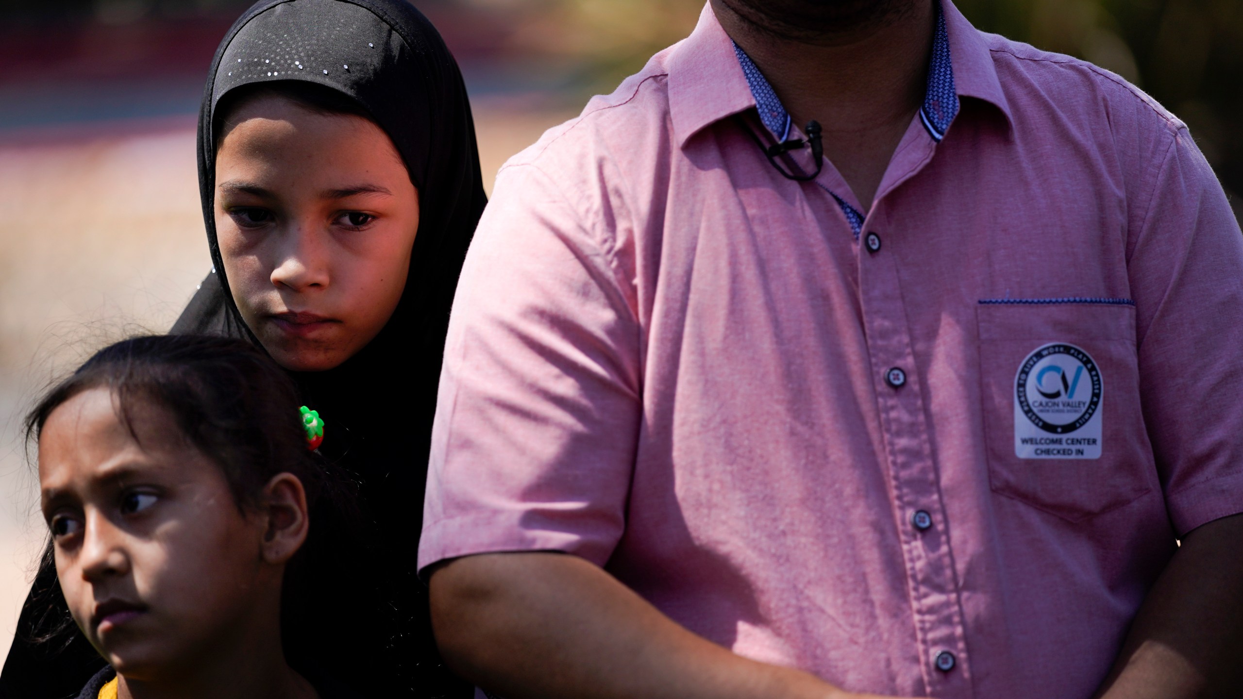 Palwasha Faizi, 10, above left, stands behind her sister, Parwana Faizi, 7, and alongside her father, Mohammad Faizi, during a news conference on Sept. 2, 2021, in El Cajon, Calif. The family were visiting relatives in Afghanistan in August, and were forced to escape as the Taliban seized power. (Gregory Bull / Associated Press)