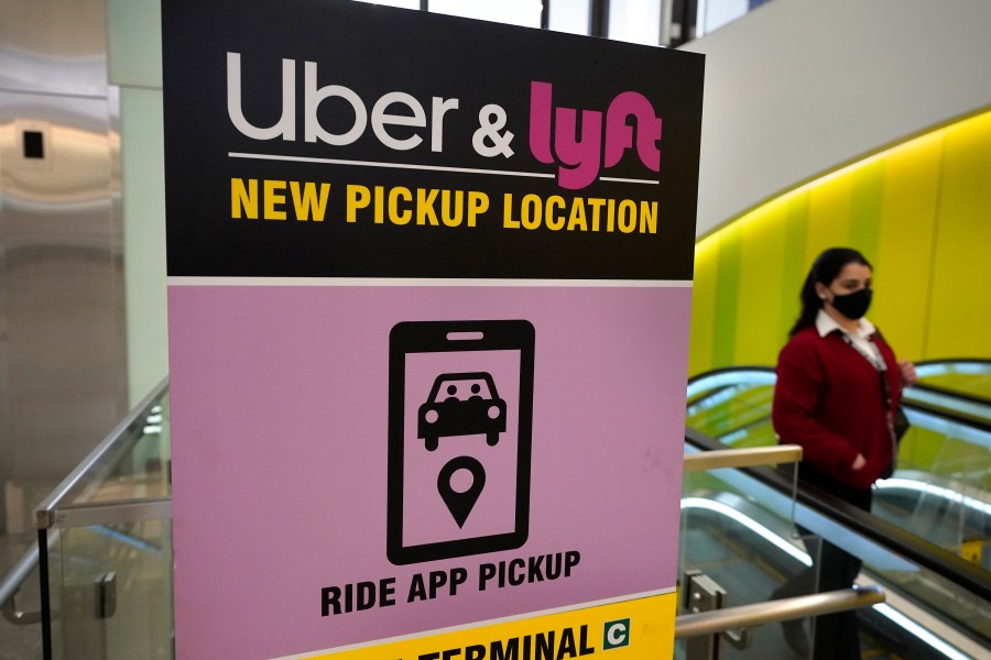 In this Feb. 9, 2021, file photo, a passer-by walks past a sign offering directions to an Uber and Lyft ride pickup location at Logan International Airport, in Boston. (AP Photo/Steven Senne, File)