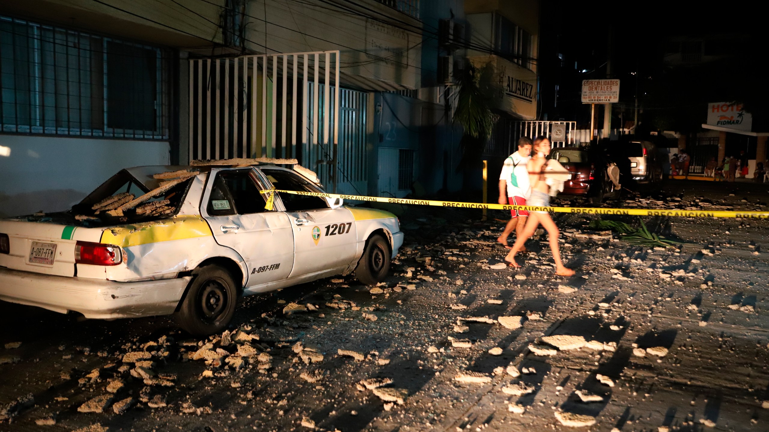 A couple walks past a taxi cab that was damaged by falling debris after a strong earthquake in Acapulco, Mexico, on Sept. 7, 2021. The quake struck southern Mexico near the resort of Acapulco, causing buildings to rock and sway in Mexico City nearly 200 miles away. (Bernardino Hernandez / Associated Press)