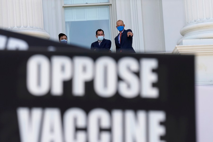 Assembly Speaker Anthony Rendon, of Lakewood, center, and Assemblyman Kevin McCarty, D-Sacramento, right, watch from the balcony outside the Assembly Chambers as protesters opposing vaccine mandates gather at the Capitol in Sacramento. (Rich Pedroncelli/Associated Press)