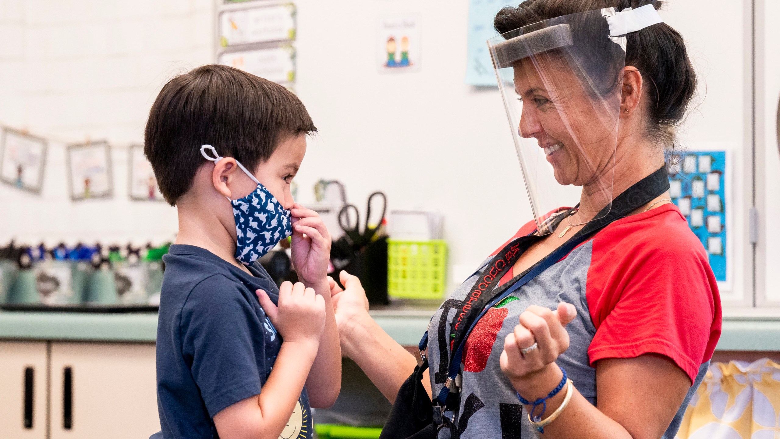 In this Aug. 12, 2021, file photo, a student gets help with his mask from transitional kindergarten teacher Annette Cuccarese during the first day of classes at Tustin Ranch Elementary School in Tustin, Calif. Now that California schools have welcomed students back to in-person learning, they face a new challenge: A shortage of teachers and all other staff, the likes of which some districts say they've never seen. (Paul Bersebach/The Orange County Register via AP, File)