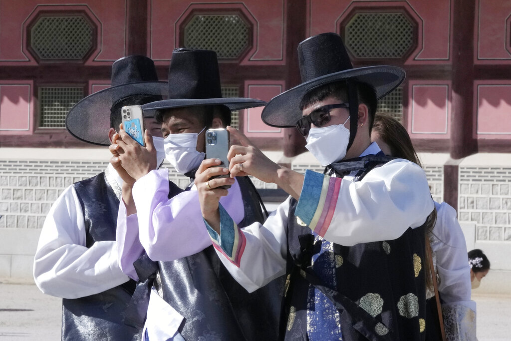 Men wearing face masks as a precaution against the coronavirus take photos as they visit to celebrate Chuseok holidays, the Korean version of Thanksgiving Day, at the Gyeongbok Palace in Seoul, South Korea, Wednesday, Sept. 22, 2021. (AP Photo/Ahn Young-joon)