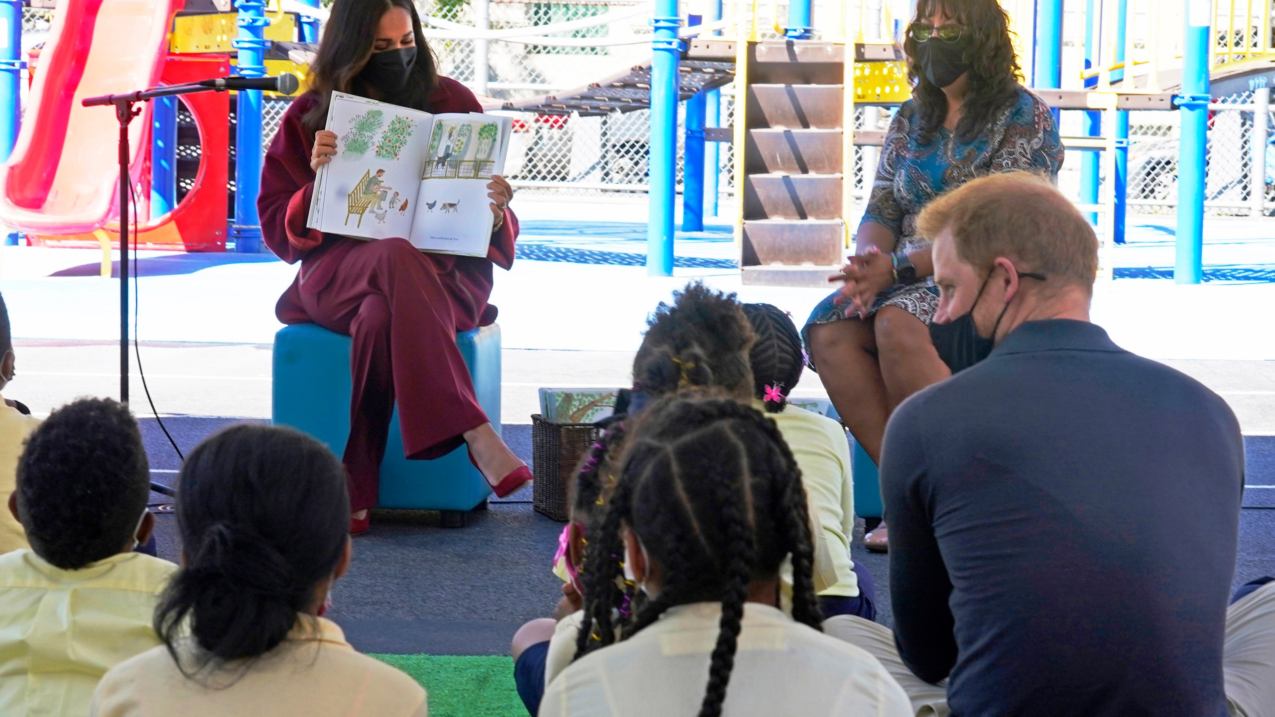 Meghan, the Duchess of Sussex, reads from her book "The Bench," as Prince Harry, the Duke of Sussex, foreground right, and second grade students listen, during their visit to P.S. 123, the Mahalia Jackson School, in New York's Harlem neighborhood on Sept. 24, 2021. (AP Photo/Richard Drew)