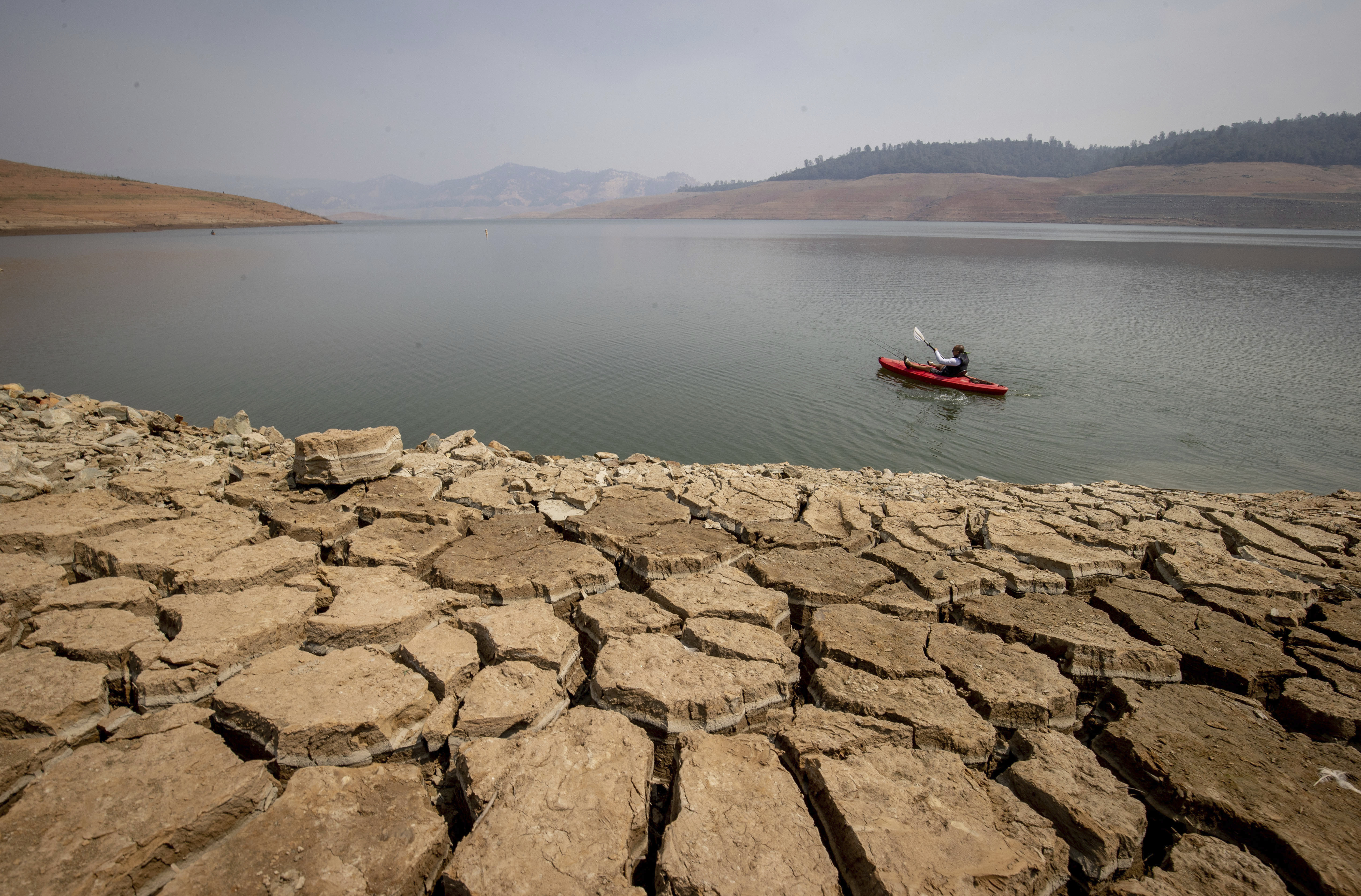 A kayaker fishes in Lake Oroville as water levels remain low due to continuing drought conditions on Aug. 22, 2021. (Ethan Swope / Associated Press)