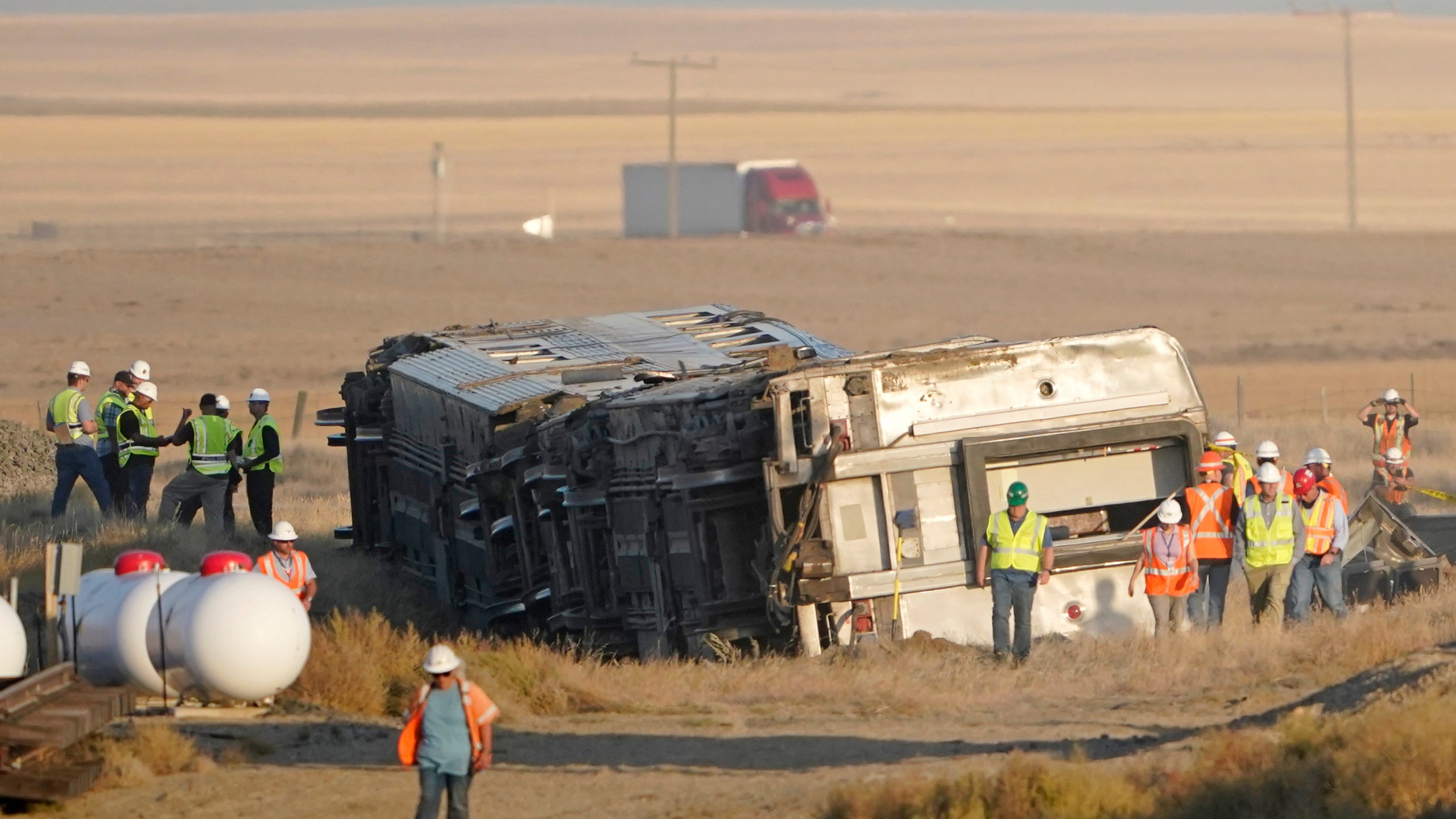 Workers stand Sunday, Sept. 26, 2021, near toppled cars from an Amtrak train that derailed Saturday, just west of Joplin, Mont. The westbound Empire Builder was en route to Seattle from Chicago with two locomotives and 10 cars. (AP Photo/Ted S. Warren)