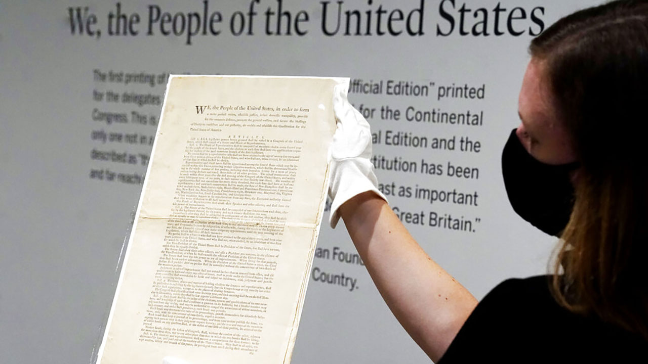 Ella Hall, a specialist in Books and Manuscripts at Sotheby's, in New York, holds a 1787 printed copy of the U.S. Constitution, Friday, Sept. 17, 2021. Sotheby's announced Friday — appropriately on Constitution Day — that in November it will put up for auction one of just 11 surviving copies of the Constitution from the official first printing produced for the delegates to the Constitutional Convention and for the Continental Congress. It's the only copy that remains in private hands and has an estimate of $15 million-$20 million. (AP Photo/Richard Drew)