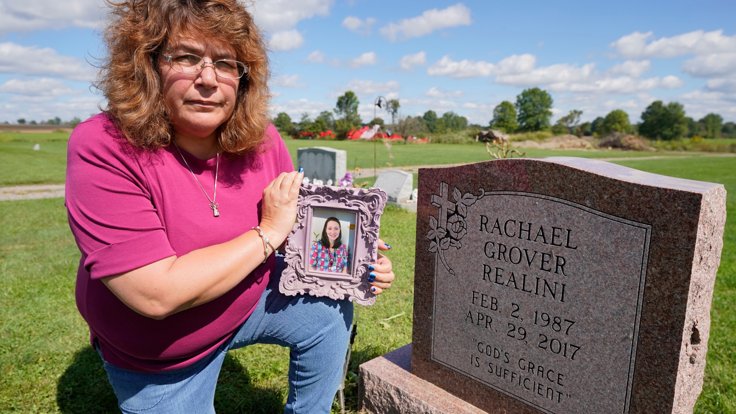 Sharon Grover holds a photograph of her daughter, Rachael, over the gravesite at Fairview Cemetery, Tuesday, Sept. 28, 2021, in Mesopotamia, Ohio. Grover believes her daughter started using prescription painkillers around 2013 but missed any signs of her addiction as her daughter, the oldest of five children, remained distanced. (AP Photo/Tony Dejak)