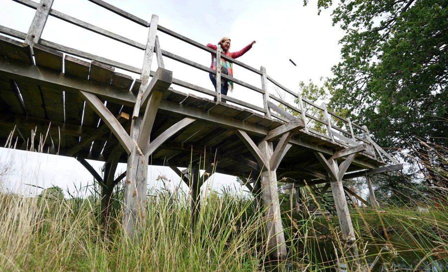 Silke Lohmann of Summers Place Auctions stands on the original Poohsticks Bridge from Ashdown Forest, featured in A.A. Milne's Winnie the Pooh books and E.H. Shepard's illustrations, near its original location in Tonbridge, Kent, England, Thursday, Sept. 30, 2021. (Gareth Fuller/PA via AP)