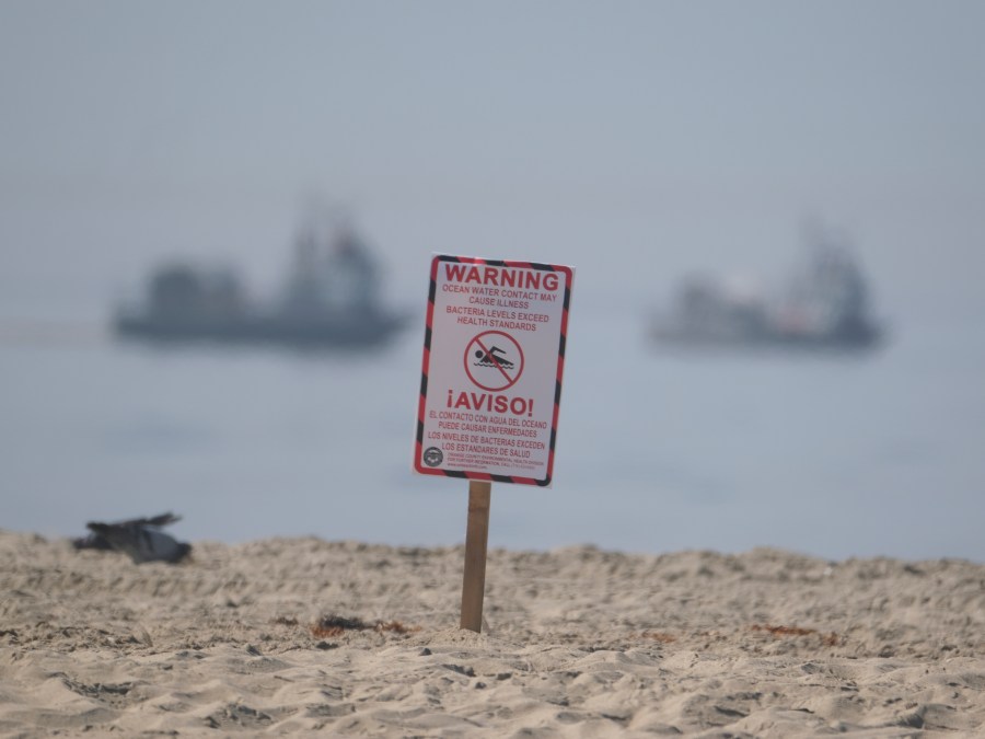 A posted sign warning about water contact may cause illness is posted by life guards after an oil spill in Huntington Beach, Calif., Sunday, Oct. 3, 2021. Vessels with the Marine Spill Response Corporation (MSRC) vessel, background, an oil spill removal organization (OSRO), deploy floating barriers around the largest oil spills in recent Southern California history fouled popular beaches and killed wildlife while crews scrambled Sunday to contain the crude before it spread further into protected wetlands. (AP Photo/Ringo H.W. Chiu)