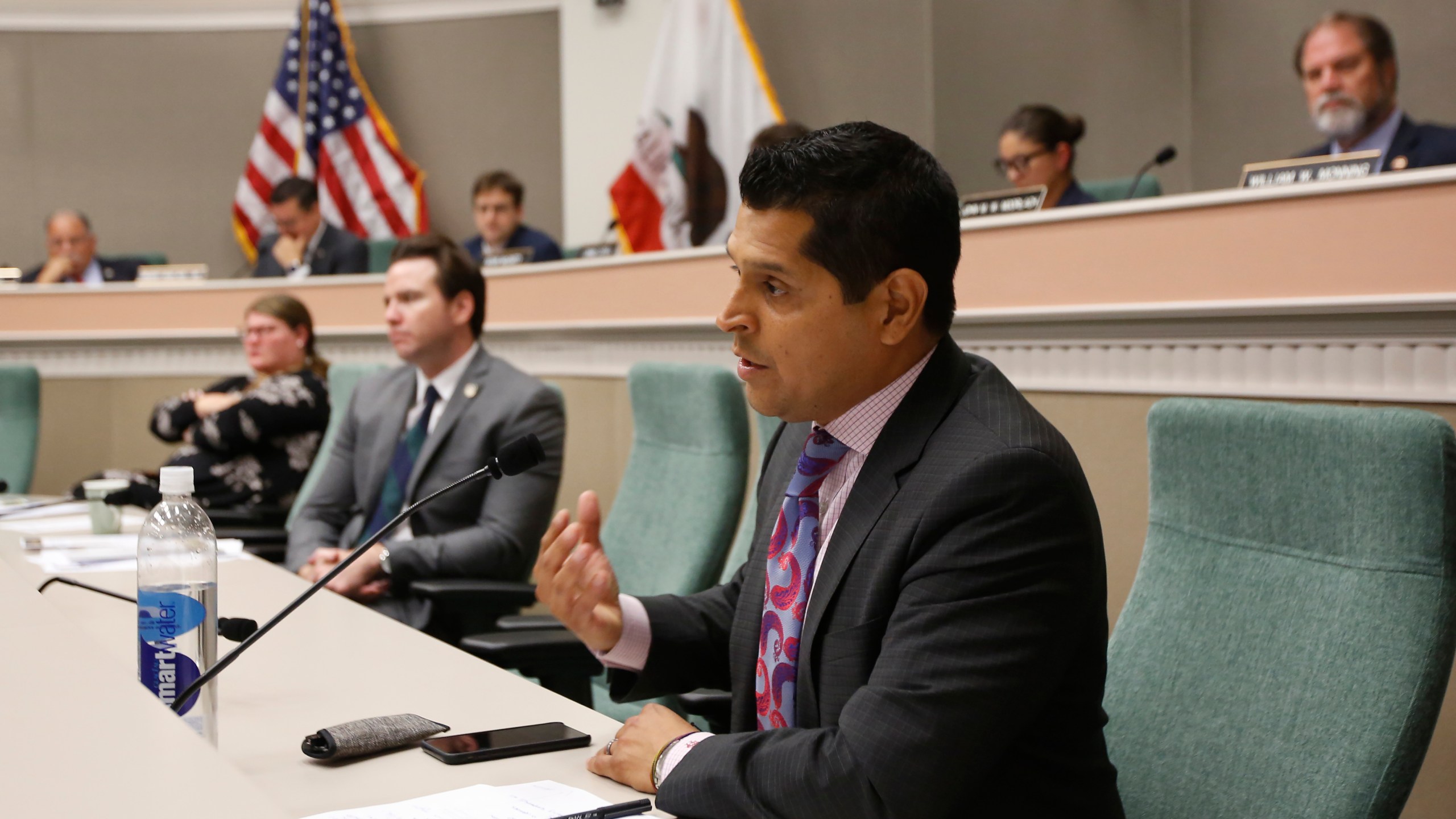 In this Aug. 12, 2019 file photo Assemblyman Miguel Santiago, D-Los Angeles, questions State Auditor Elaine Howle about an audit her office performed, during a hearing in Sacramento, Calif. Gov. Gavin Newsom signed a measure authored by Santiago that will let some adult children add their parents as dependents on their health insurance plans. The law would not apply to people who get health insurance through their work and only apply to people who purchase their own insurance on the individual market. (AP Photo/Rich Pedroncelli, File)