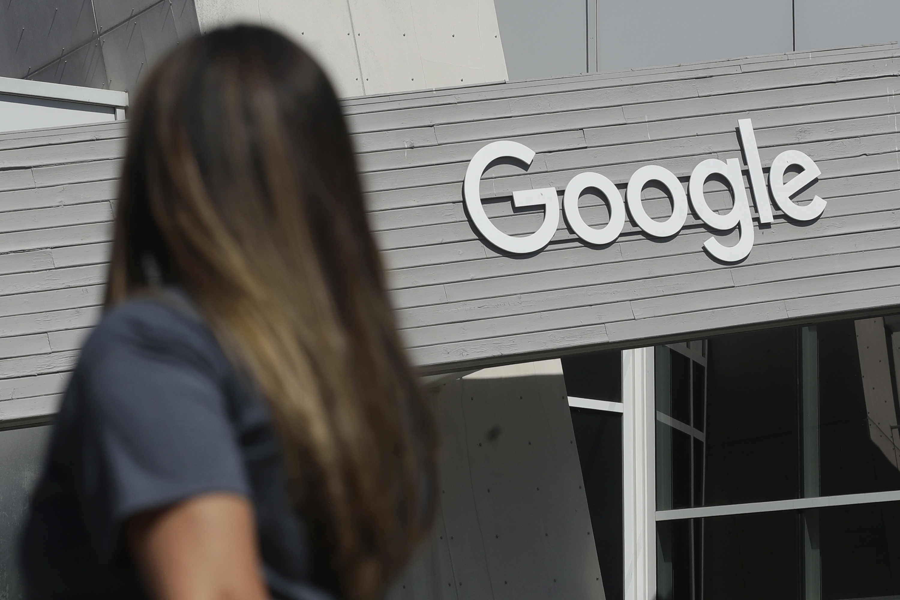 In this Sept. 24, 2019, file photo, a woman walks below a Google sign on the campus in Mountain View, Calif. Google on Thursday, Oct. 7, 2021, will no longer allow digital ads promoting false climate change claims to appear next to the content of other publishers, hoping to deny money to those making such claims and to stop the spread of misinformation on its platform. (AP Photo/Jeff Chiu, File)