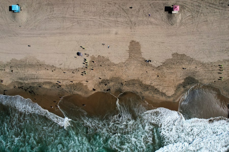 This Monday, Oct. 11, 2021, aerial file photo taken with a drone, shows beachgoers as workers in protective suits continue to clean the contaminated beach in Huntington Beach, Calif. The amount of crude oil spilled in an offshore pipeline leak in Southern California is believed to be close to about 25,000 gallons, a Coast Guard official said Thursday Oct. 14, 2021. (AP Photo/Ringo H.W. Chiu, File)