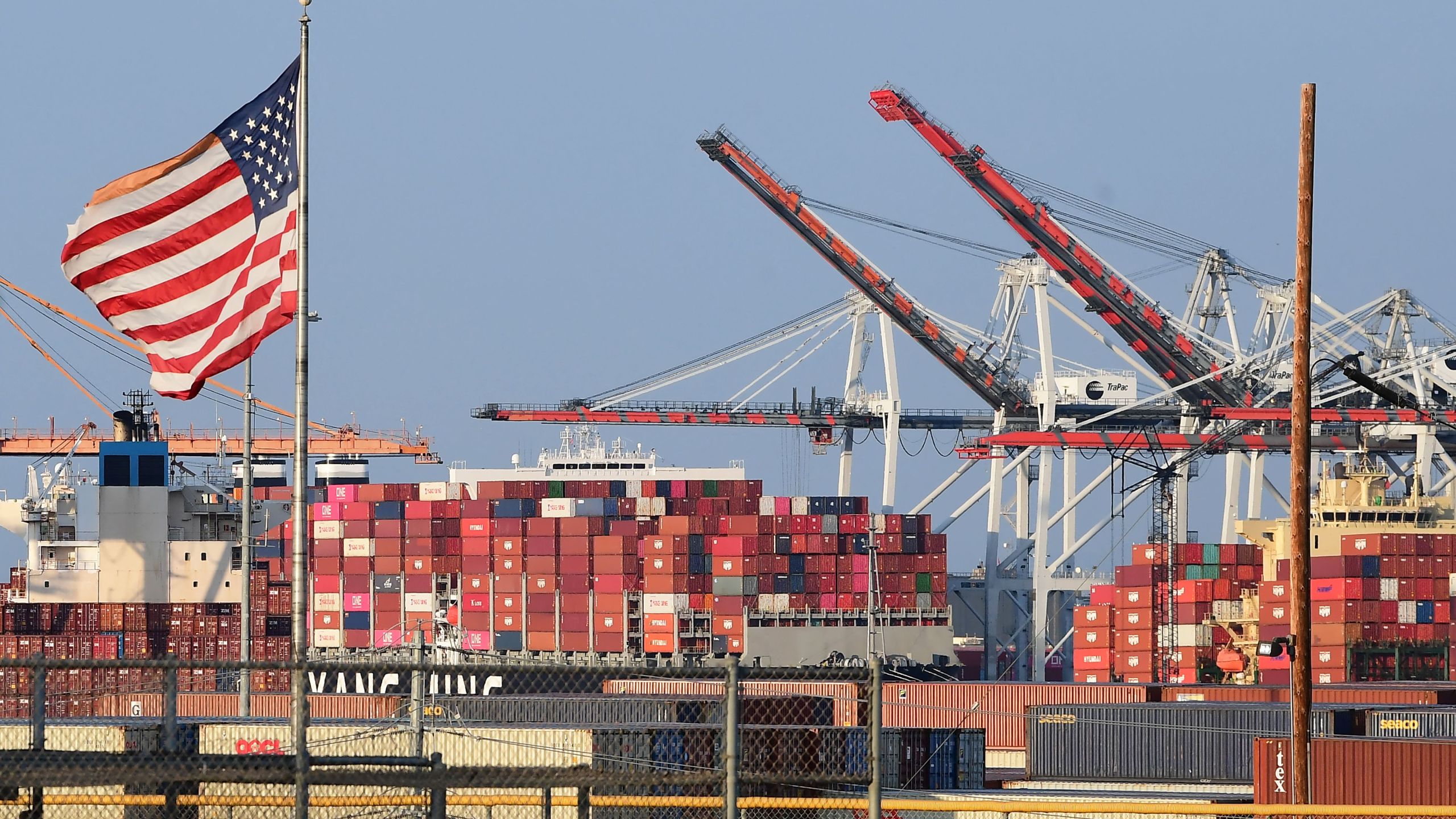 A US flag flies near containers stacked high on a cargo ship at the Port of Los Angeles on September 28, 2021 in Los Angeles, California. - A record number of cargo ships are stuck floating and waiting off the southern California coast amid a supply chain crisis which could mean fewer gifts and toys for Christmas this year as a combination of growing volumes of cargo, Covid-19 related saftey measures and a labor shortage slow the handling and processing of cargo from each ship. (Photo by Frederic J. BROWN / AFP) (Photo by FREDERIC J. BROWN/AFP via Getty Images)