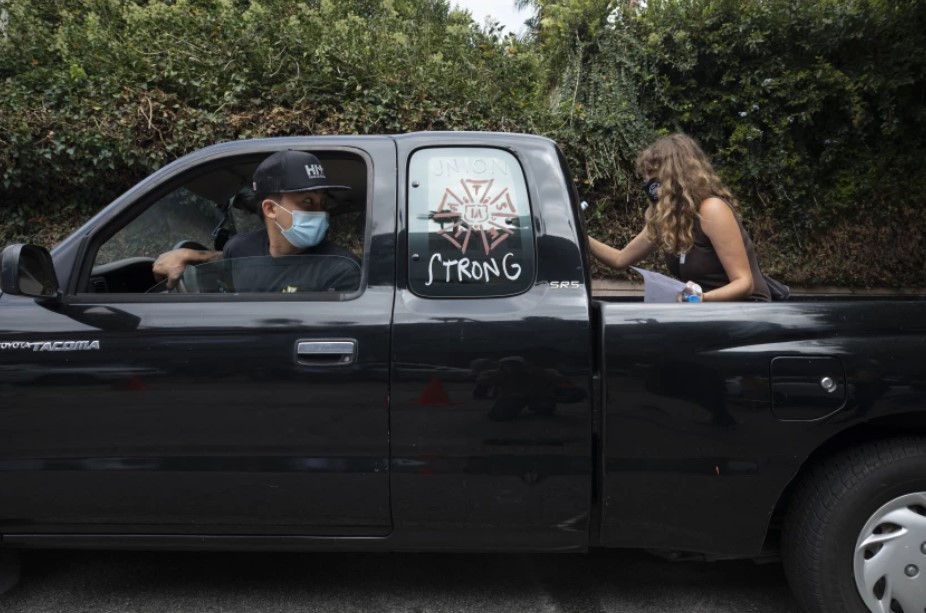 Kevin Chiu of IATSE Local 80, which represents grips and other set workers, waits in his car as volunteer Liz Lipschultz writes pro-labor slogans during a rally at the Motion Picture Editors Guild IATSE Local 700 on Sept. 26, 2021, in Los Angeles. (Myung J. Chun/Los Angeles Times)