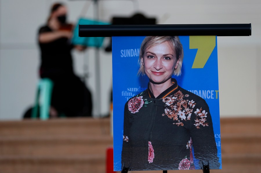 A musician plays a violin behind a photograph of cinematographer Halyna Hutchins during a vigil in her honor in Albuquerque, N.M., Saturday, Oct. 23, 2021. Hutchins was fatally shot on Thursday, Oct. 21, after an assistant director unwittingly handed actor Alec Baldwin a loaded weapon and told him it was safe to use on the set of a Western filmed in Santa Fe, N.M. (AP Photo/Andres Leighton)