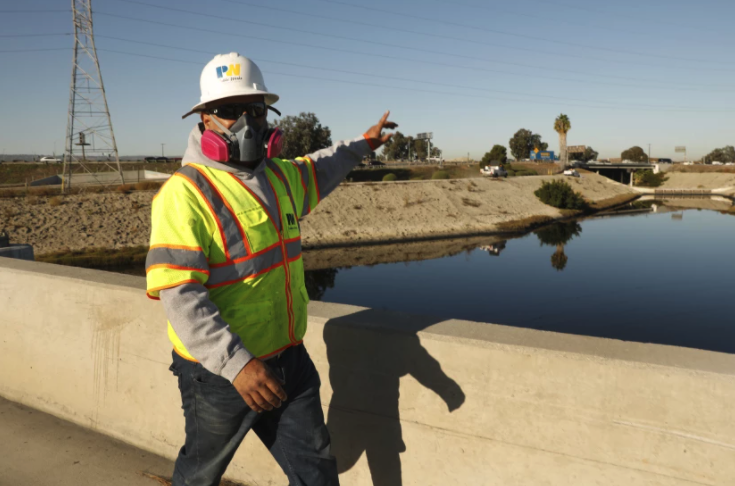 A crew member from the Los Angeles County Department of Public Works, wearing a mask to block out the noxious smell, prepares to work on the Dominguez Channel in Carson.(Carolyn Cole / Los Angeles Times)