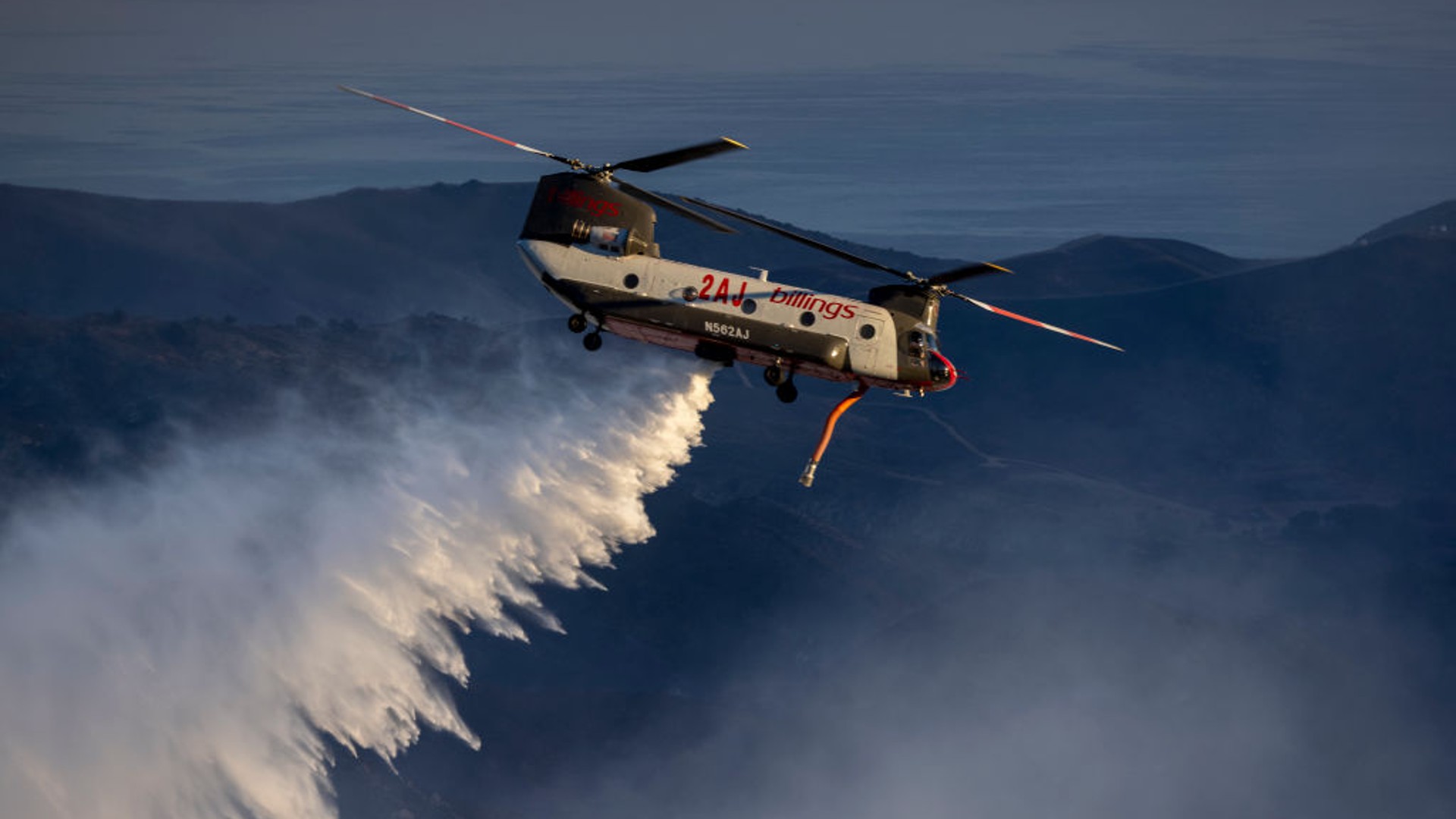 A firefighting helicopter makes a water drop as the Alisal Fire burns on October 13, 2021 near Goleta, California. (David McNew/Getty Images)