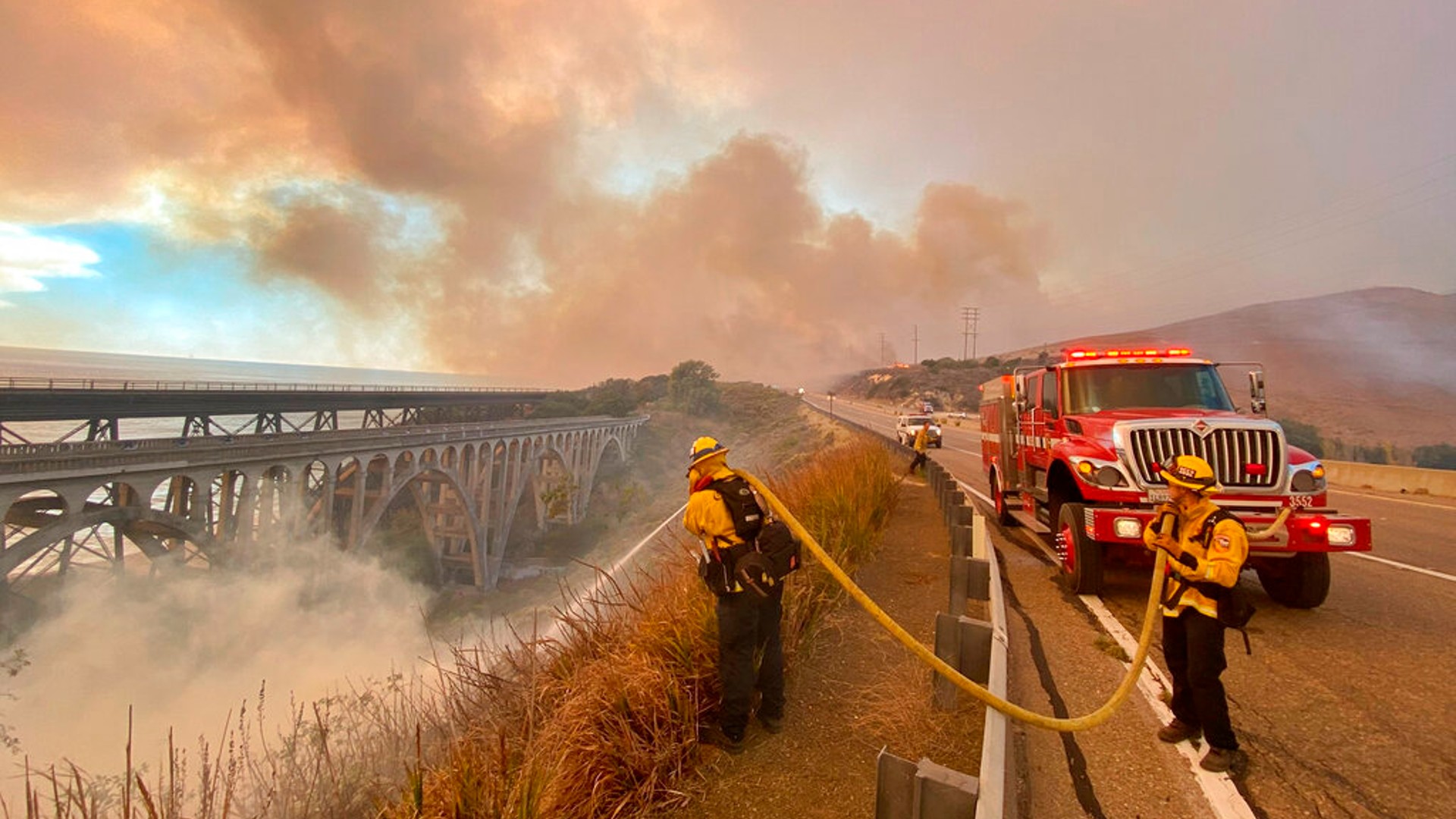 In this photo provided by the Santa Barbara County Fire Department, firefighters extinguish flames Tuesday afternoon, Oct. 12, 2021, that have spotted ahead of the fire front along Highway 101 southbound at Vista Point, north of Refugio State Beach in Santa Barbara County, Calif. (Mike Eliason/Santa Barbara County Fire Department via AP)