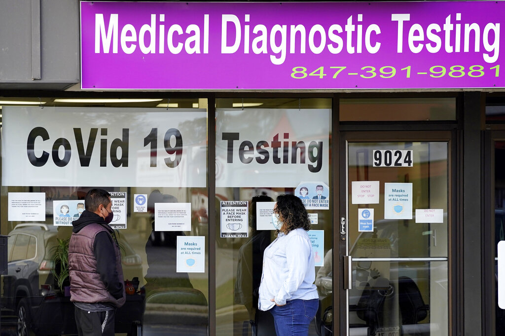 In this Oct. 21, 2020, file photo, an Exam Corp Lab employee, right, wears a mask as she talks with a patient lined up for COVID-19 testing in Niles, Ill. (AP Photo/Nam Y. Huh, File)