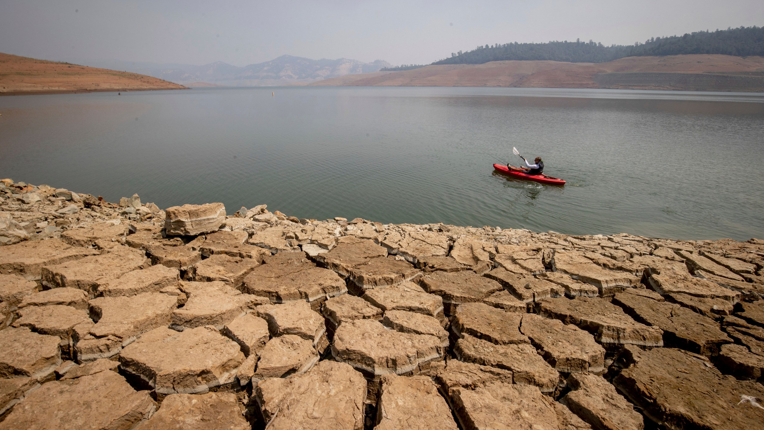 A kayaker fishes in Lake Oroville as water levels remain low due to continuing drought conditions in Oroville, Calif., on Aug. 22, 2021. (AP Photo/Ethan Swope, File)