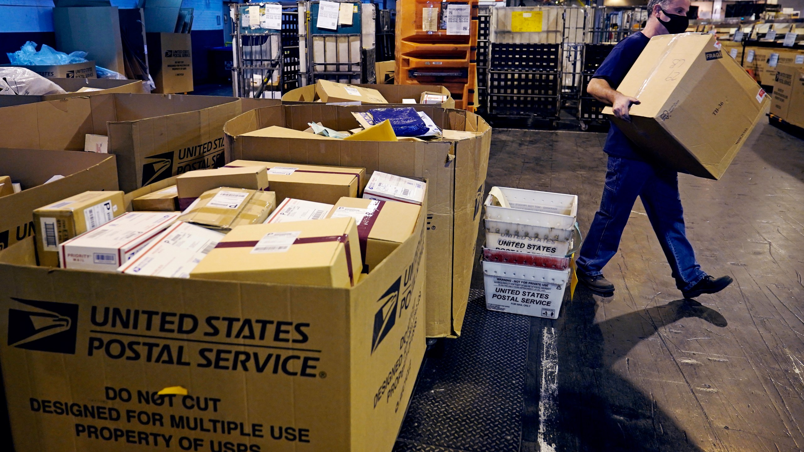 A worker carries a large parcel at the United States Postal Service sorting and processing facility, Thursday, Nov. 18, 2021, in Boston. Last year's holiday season was far from the most wonderful time of the year for the beleaguered U.S. Postal Service. Shippers are now gearing up for another holiday crush.(AP Photo/Charles Krupa)