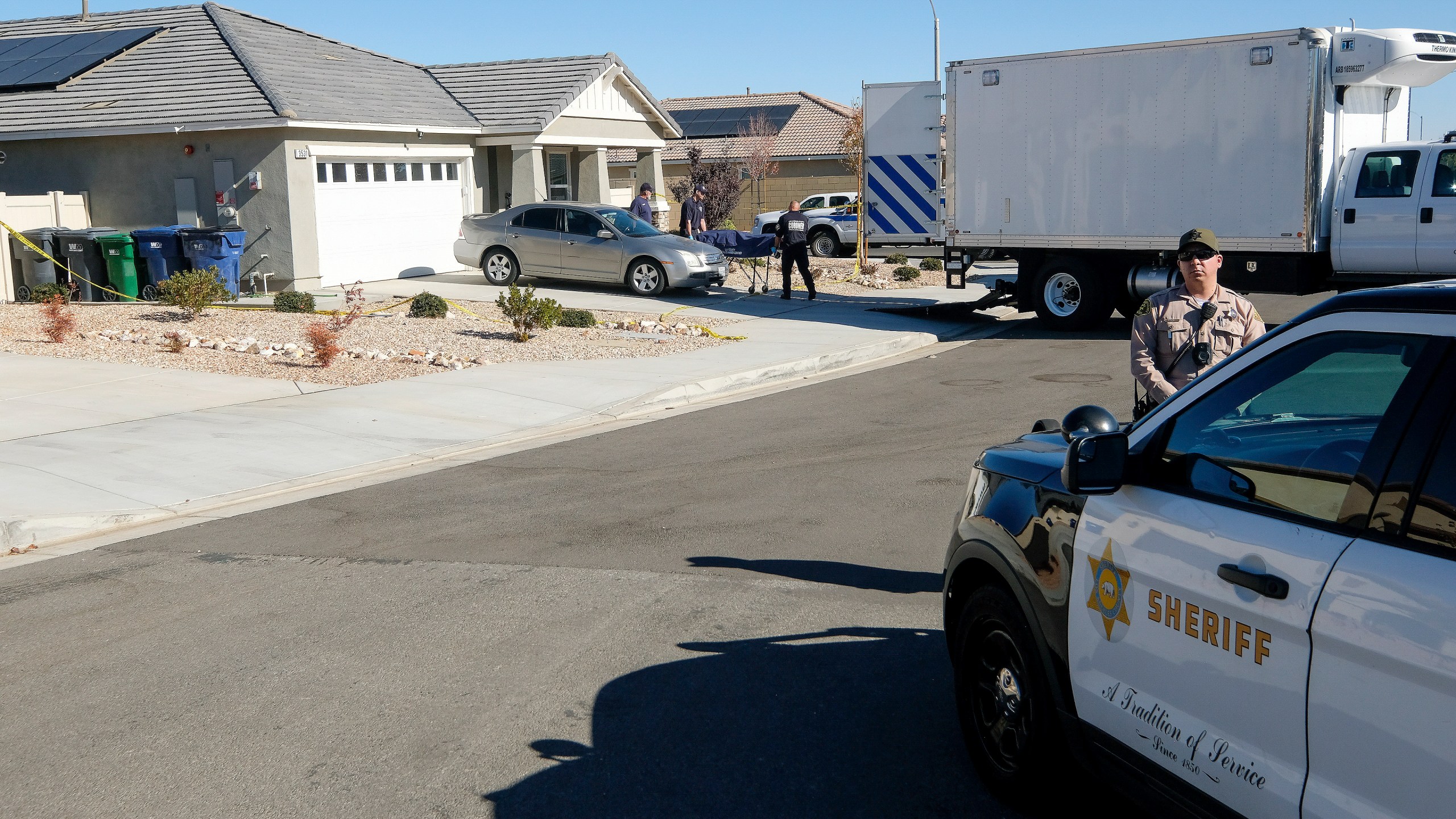 Los Angeles County Coroner officials remove a body from a home where five bodies were found dead, in the city of Lancaster in the high desert Antelope Valley north of Los Angeles, Monday, Nov. 29, 2021. A Los Angeles County Sheriff's Department statement says deputies found a woman, a girl and three boys with gunshot wounds and paramedics pronounced them dead at the scene. The department says the children's father showed up at the Lancaster sheriff's station and was arrested on suspicion of five murders after being interviewed by detectives. (AP Photo/Ringo H.W. Chiu)