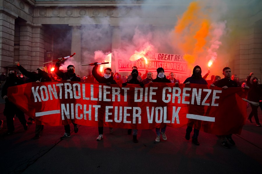 Demonstrators shout slogans and light flares during a demonstration against measures to battle the coronavirus pandemic in Vienna, Austria, Saturday, Nov. 20, 2021. Thousands of protesters are expected to gather in Vienna after the Austrian government announced a nationwide lockdown to contain the quickly rising coronavirus infections in the country. Banner reads: 'Controls the border. Not your people.' (AP Photo/Florian Schroetter)