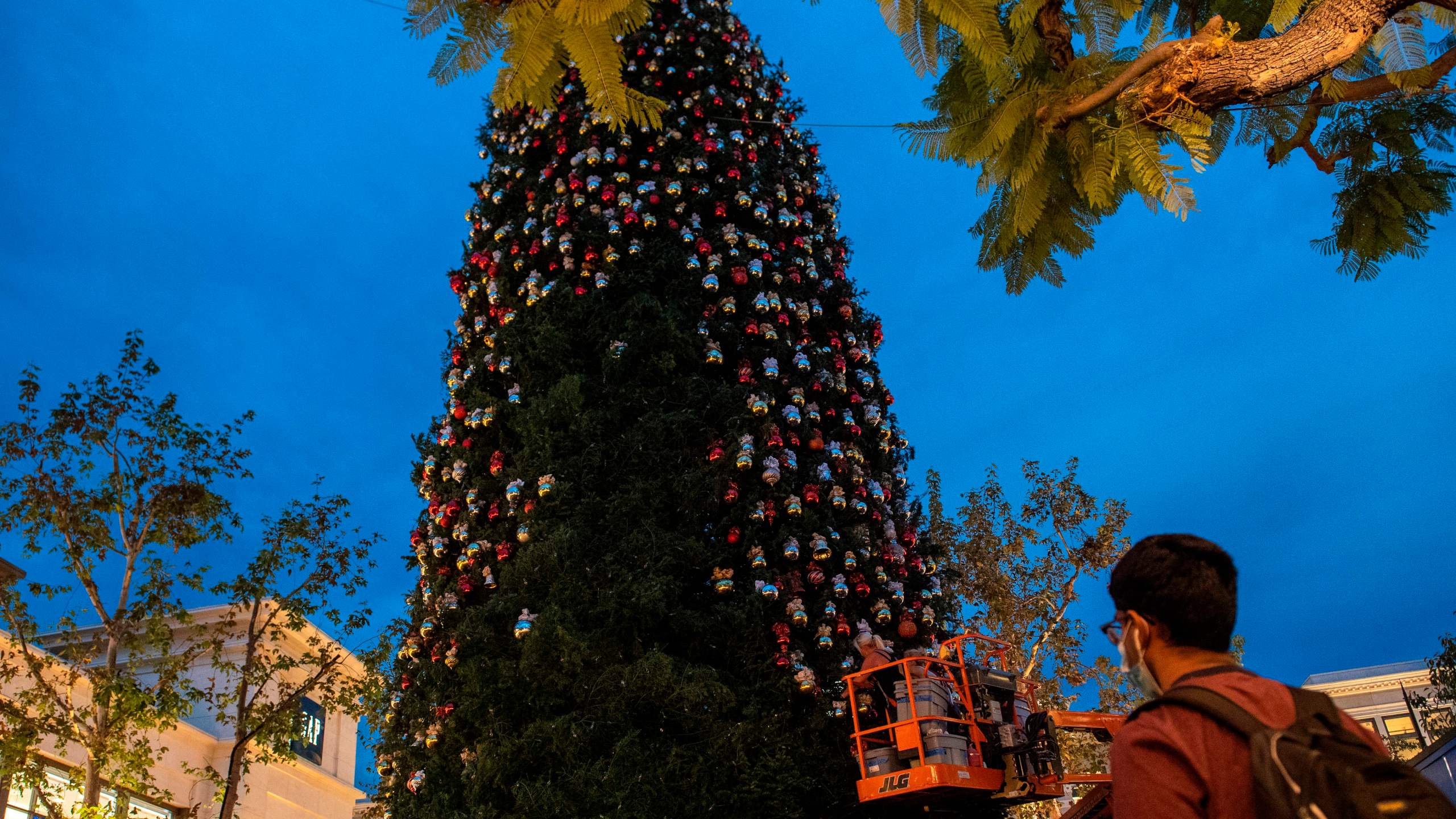 A person wearing a face mask watches a worker decorate the Christmas tree at The Grove outdoor shopping center, amid the coronavirus pandemic on Nov. 5 2020. (VALERIE MACON via Getty Images)