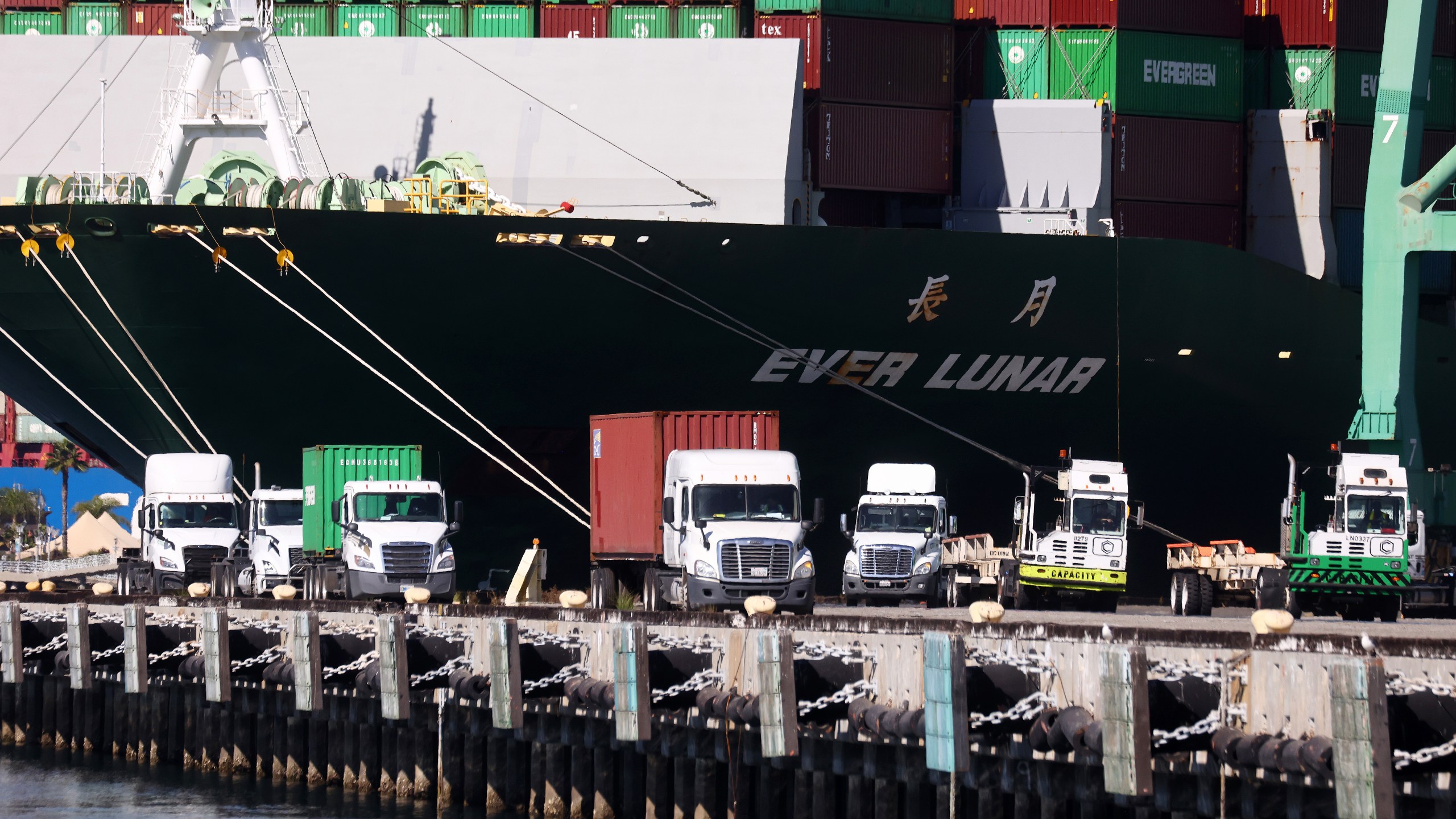 Trucks drive beneath cargo containers stacked on a container ship at the Port of Los Angeles on Oct. 15, 2021 in San Pedro. (Mario Tama/Getty Images)