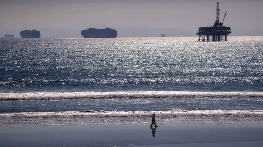 Container ships and an offshore oil rig line the horizon as an oil spill cleanup crew member walks the shoreline in Huntington Beach in October. (Allen J. Schaben/Los Angeles Times)