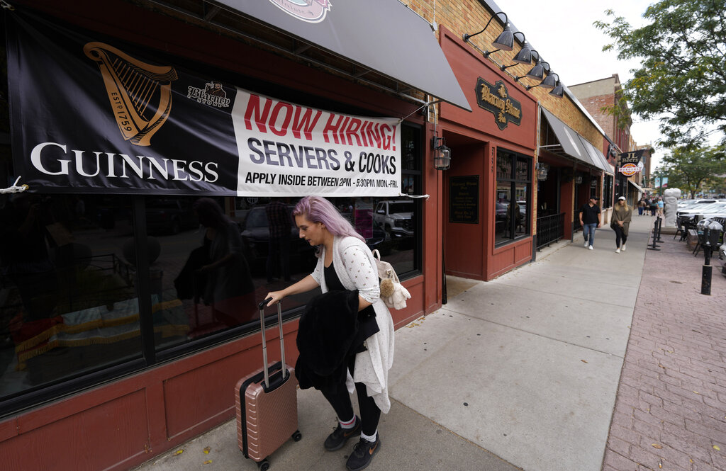 A traveller wheels her baggage past a now hiring sign outside a bar and restaurant Saturday, Oct. 9, 2021, in Sioux Falls, S.D. (AP Photo/David Zalubowski)