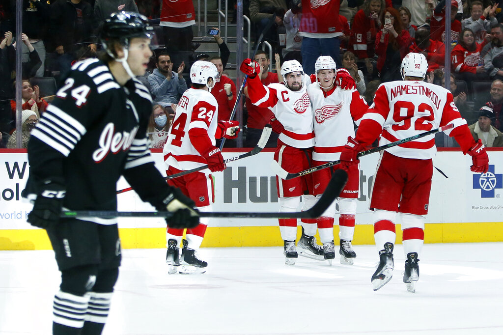 Detroit Red Wings center Dylan Larkin, third from left, celebrates his second goal of the game with center Pius Suter (24), defenseman Gustav Lindstrom and center Vladislav Namestnikov (92) as New Jersey Devils defenseman Ty Smith (24) skates off during the second period of an NHL hockey game Saturday, Dec. 18, 2021, in Detroit. (AP Photo/Duane Burleson)