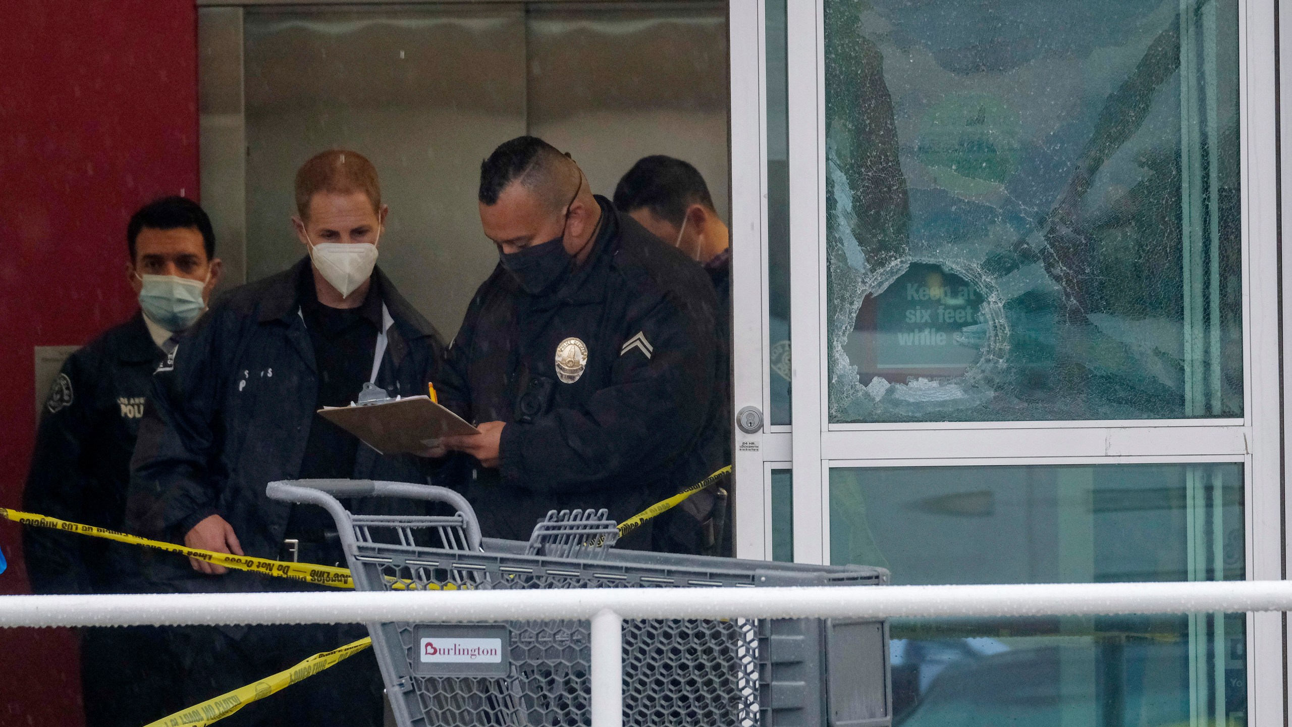 Police officers work near a broken glass door at the scene where two people were struck by gunfire in a shooting at a Burlington store — part of a chain formerly known as Burlington Coat Factory in North Hollywood, Calif., Thursday, Dec. 23, 2021. (AP Photo/Ringo H.W. Chiu)