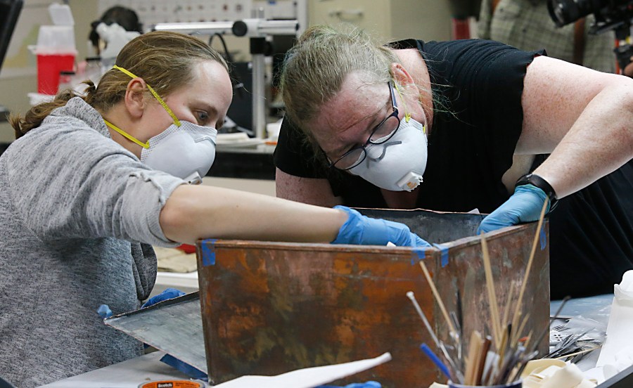 Sue Donovan, left, and Kate Ridgeway, right, dig into the artifacts inside a copper box time capsule recovered from the base of a Robert E. Lee monument, Tuesday, Dec. 28, 2021, at the Virginia Department of Historical Resources lab in Richmond, Va. (Bob Brown/Richmond Times-Dispatch via AP)