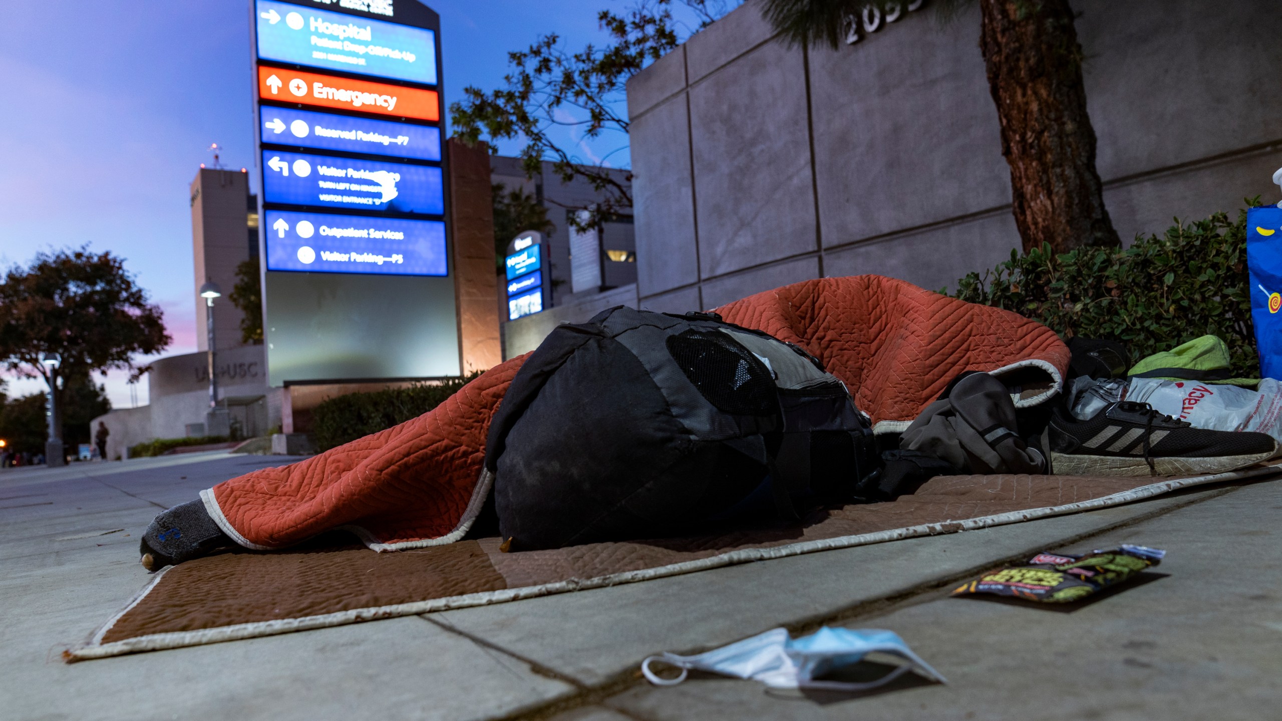 A homeless person sleeps outside the Los Angeles County+USC Medical Center entrance on Dec. 16, 2020. (AP Photo/Damian Dovarganes, File)