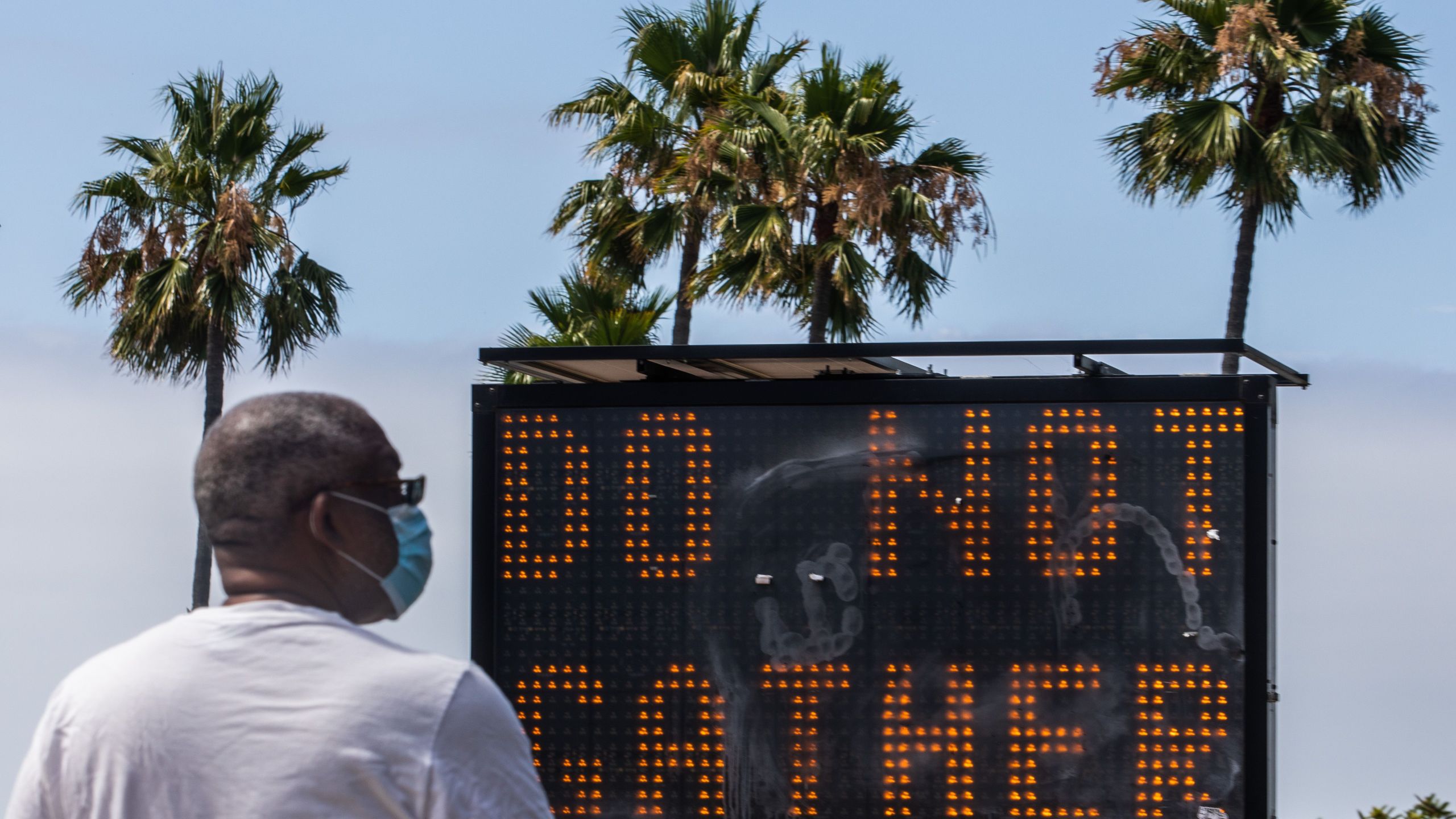 A man wearing a facemask checks his phone near a sign urging people not to gather, while he walks on the beach in Long Beach, California, on July 14, 2020. (APU GOMES/AFP via Getty Images)