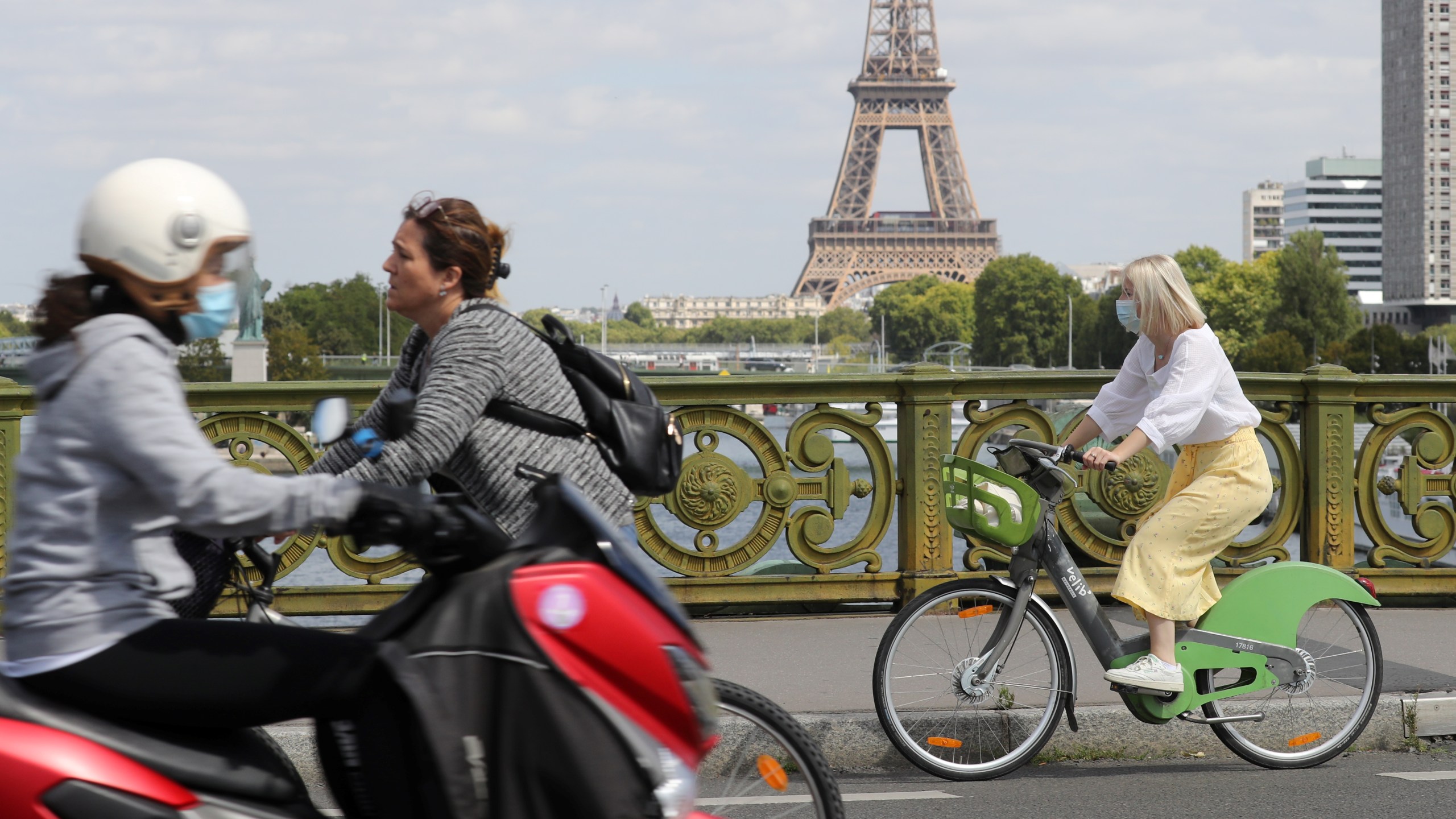 A woman wears a protective face mask while cycling across Pont Mirabeau bridge, near the Eiffel Tower, on August 27, 2020, in Paris. - France's prime minister on August 27 announced face masks will become compulsory throughout Paris, expressing concern over an "undeniable" trend of expanding coronavirus infection in the country. (Photo by Ludovic MARIN / AFP) (Photo by LUDOVIC MARIN/AFP via Getty Images)