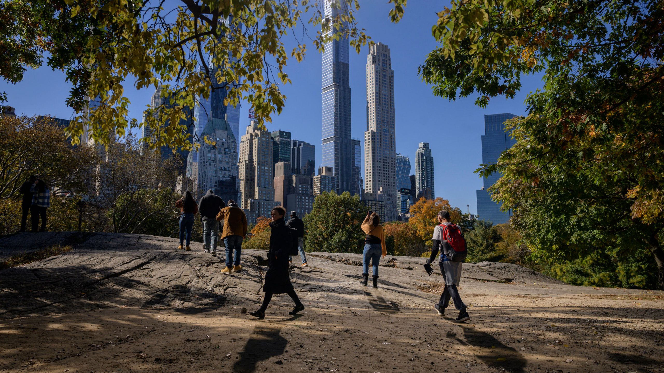 People stand beneath fall foliage and before high-rise buildings of the Manhattan city skyline in Central Park in New York on Nov. 5, 2021. (ED JONES/AFP via Getty Images)