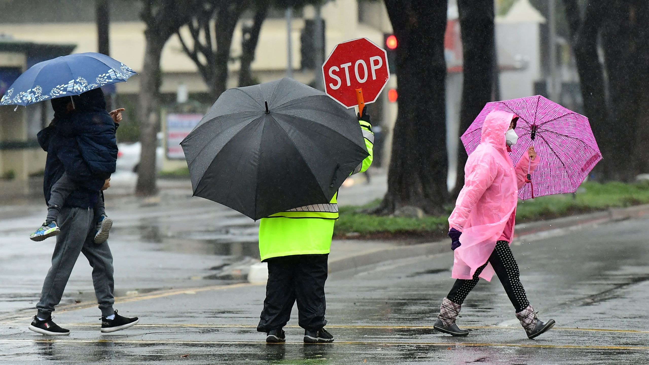 A school crossing guard holds a Stop sign for vehicular traffic as pedestrians cross a road in the rain on Dec. 14, 2021 in Monterey Park, California. (FREDERIC J. BROWN/AFP via Getty Images)